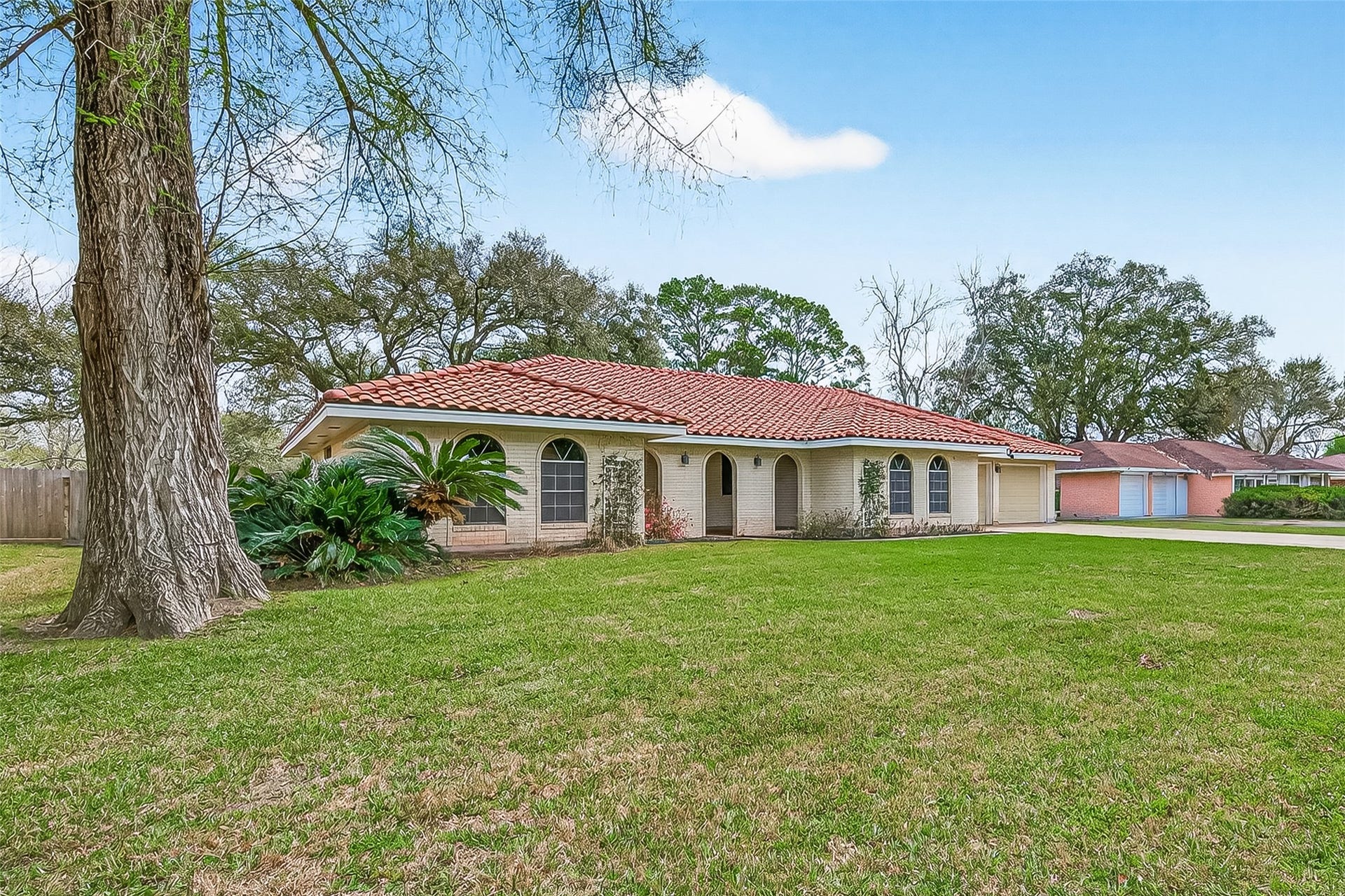 5607 Avenue M 1/2, Santa Fe, TX 77510 This charming home features a red-tiled roof and light brick exterior, set on a spacious, grassy lot with mature trees. The curved windows and arched entryway add character