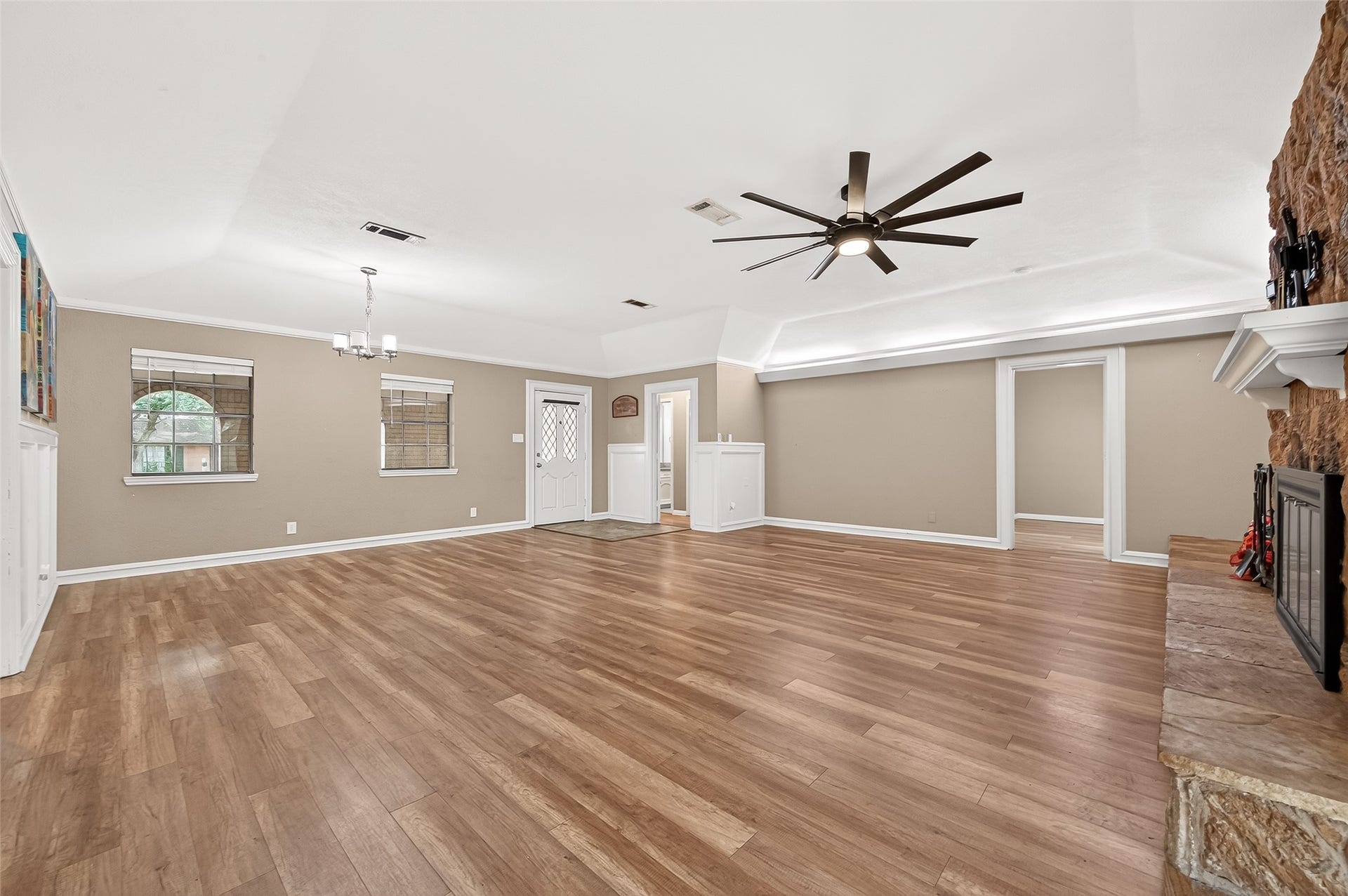5607 Avenue M 1/2, Santa Fe, TX 77510 Spacious living room with wood flooring, neutral walls, and a ceiling fan. Features a stone fireplace and ample natural light from multiple windows. Includes an elegant chandelier and access to adjacent rooms.