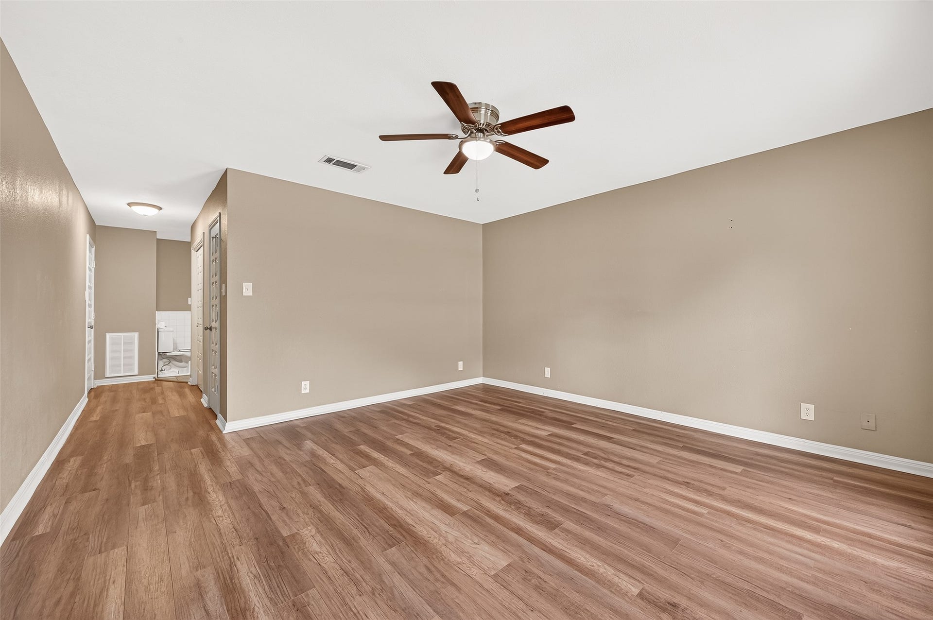 5607 Avenue M 1/2, Santa Fe, TX 77510 This primary bedroom features warm wood flooring, neutral walls, and a ceiling fan, creating a comfortable and inviting atmosphere. The open layout offers versatility for various furniture arrangements.