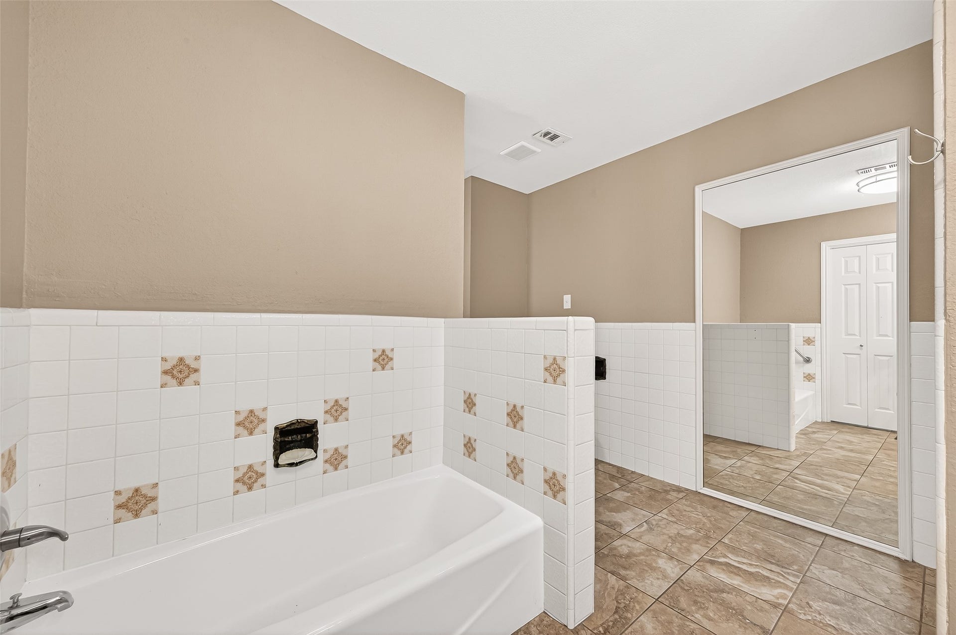 5607 Avenue M 1/2, Santa Fe, TX 77510 This bathroom features a spacious layout with a large bathtub, tiled walls with decorative accents, and a full-length mirror. The neutral color palette and tiled floor create a clean and modern look.