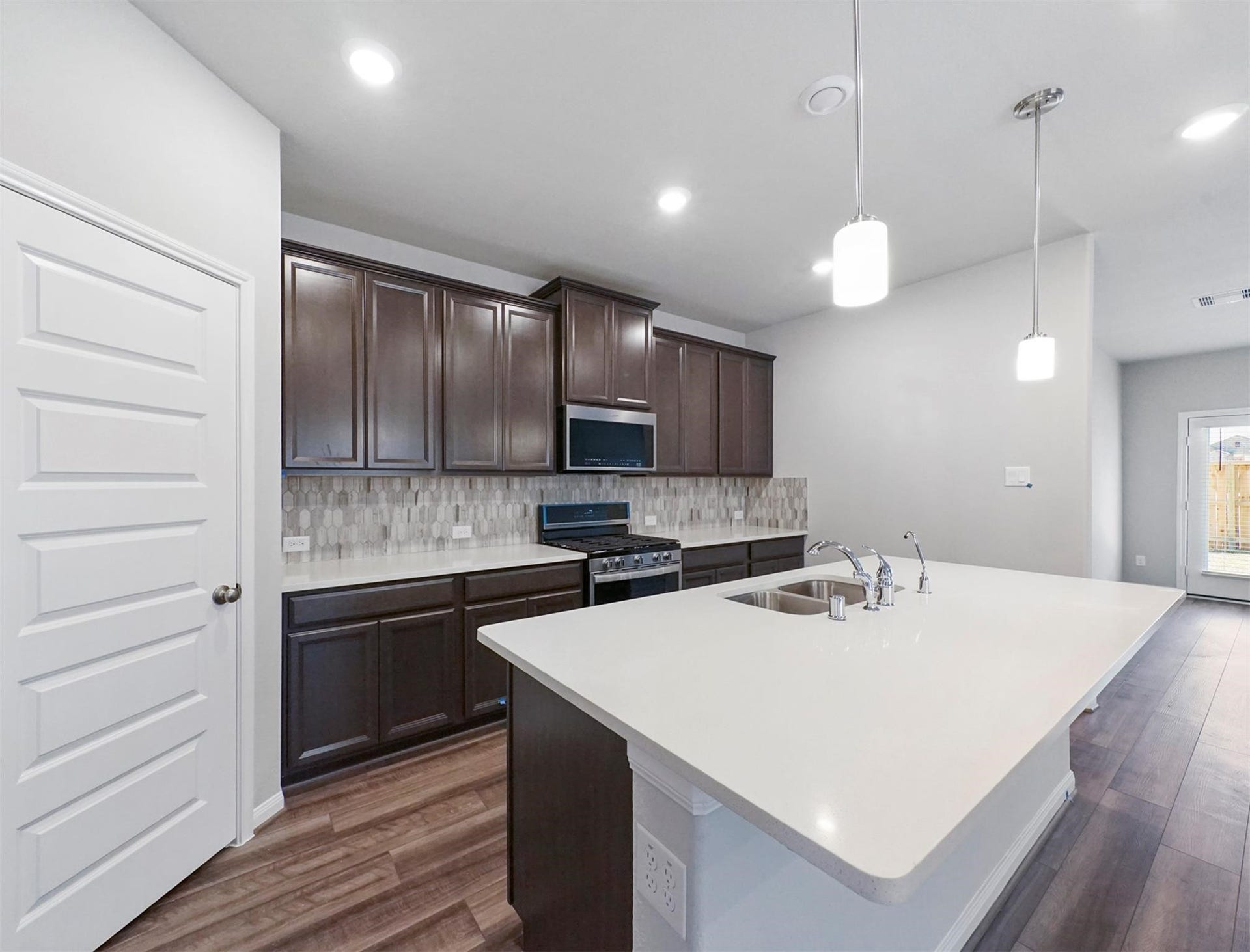 Sleek and modern kitchen with dark cabinetry, bright countertops, tile backsplash, and a large island with pendant lighting and sink.