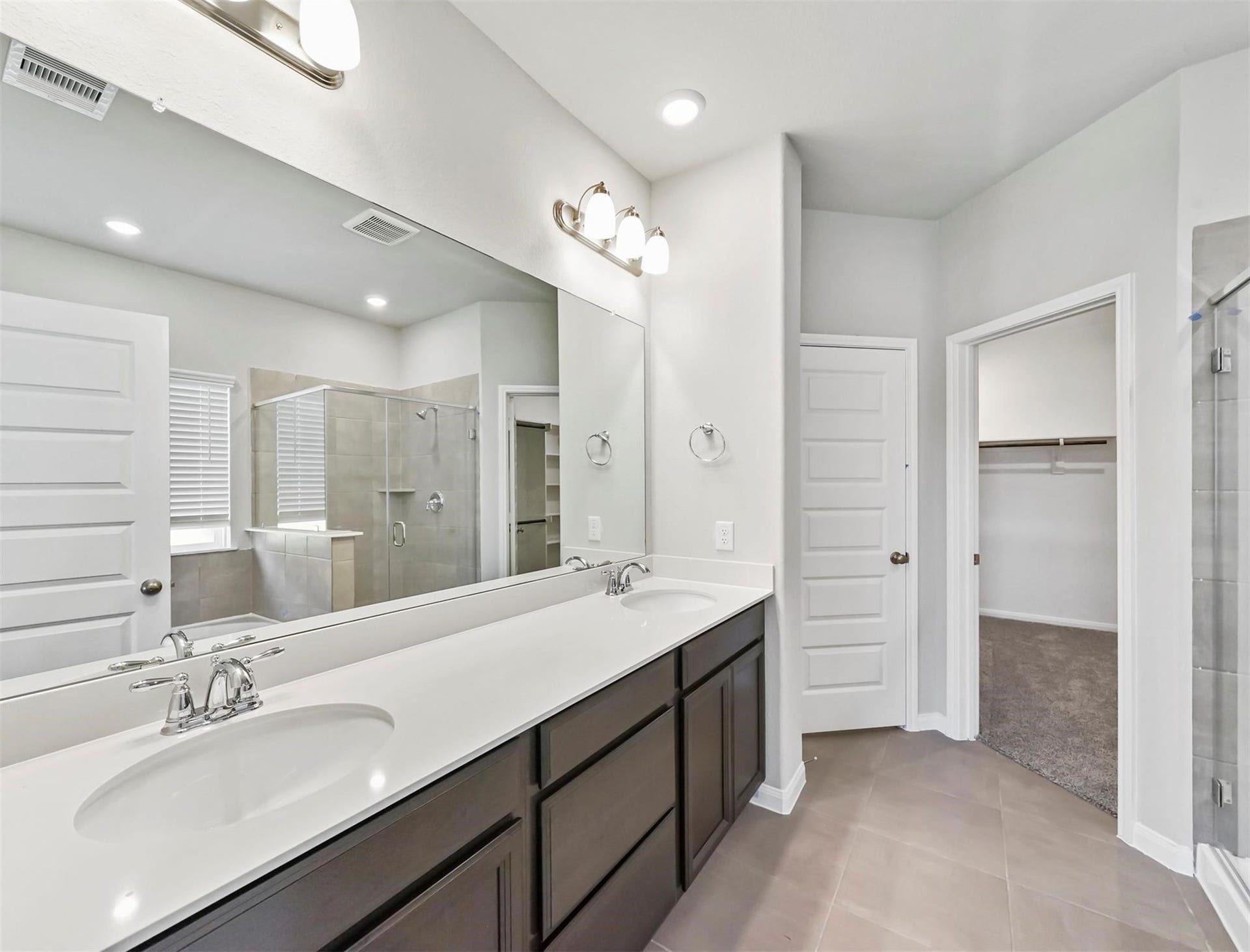 The spa-inspired primary bathroom features dual vanities, oversized mirror, and direct access to a spacious walk-in closet.