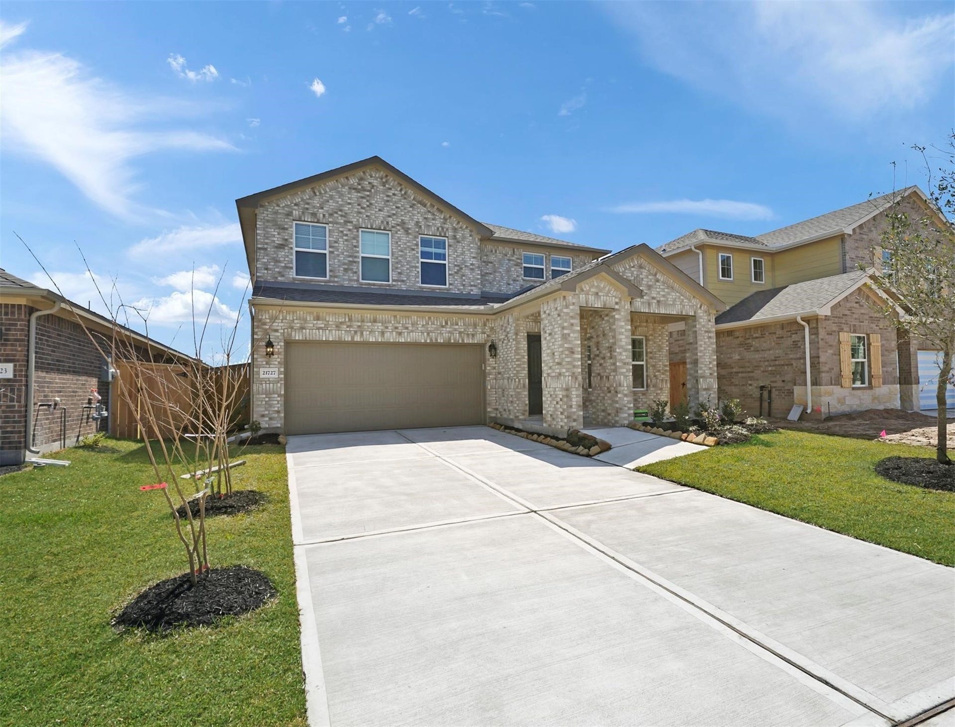 Charming two-story brick and stone exterior with a two-car garage, lush landscaping, and a spacious driveway.