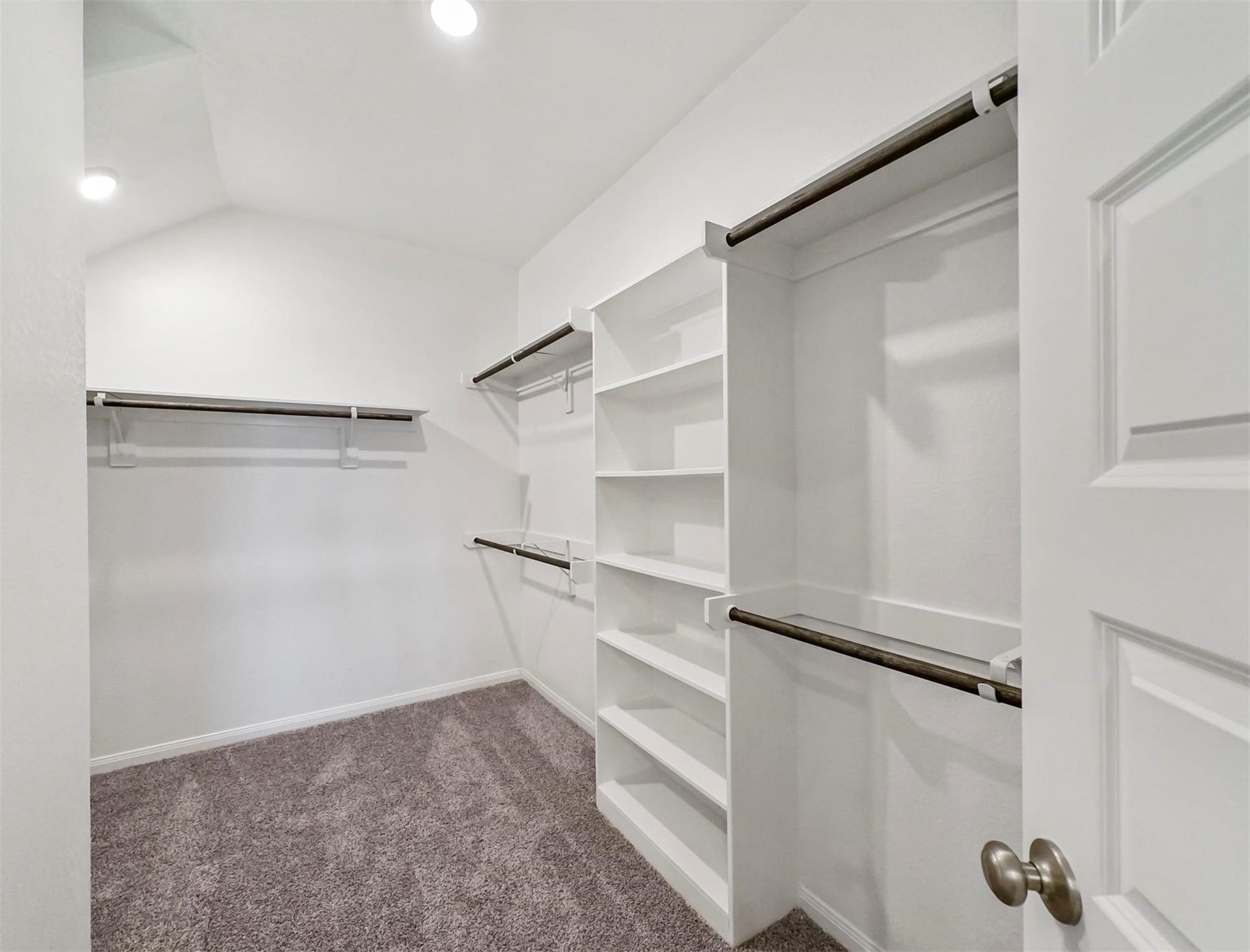 Expansive walk-in closet featuring built-in shelves, dual hanging rods, and soft carpet flooringdesigned for maximum organization and storage.