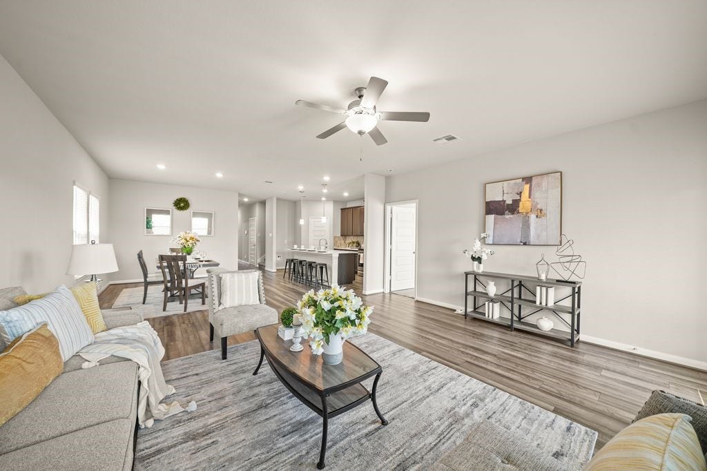 Light-filled living room features large windows, a ceiling fan, and a cozy layout ideal for relaxing or entertaining guests.