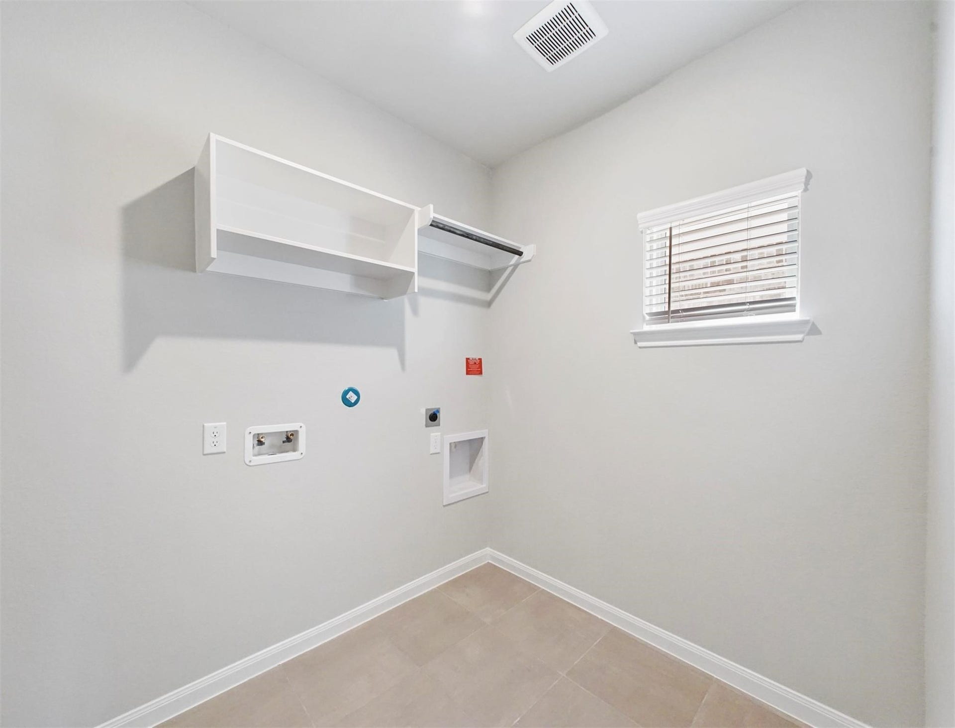 Dedicated laundry room with built-in shelving, tile flooring, and a window for natural lightfunctional and ready for your washer and dryer setup.