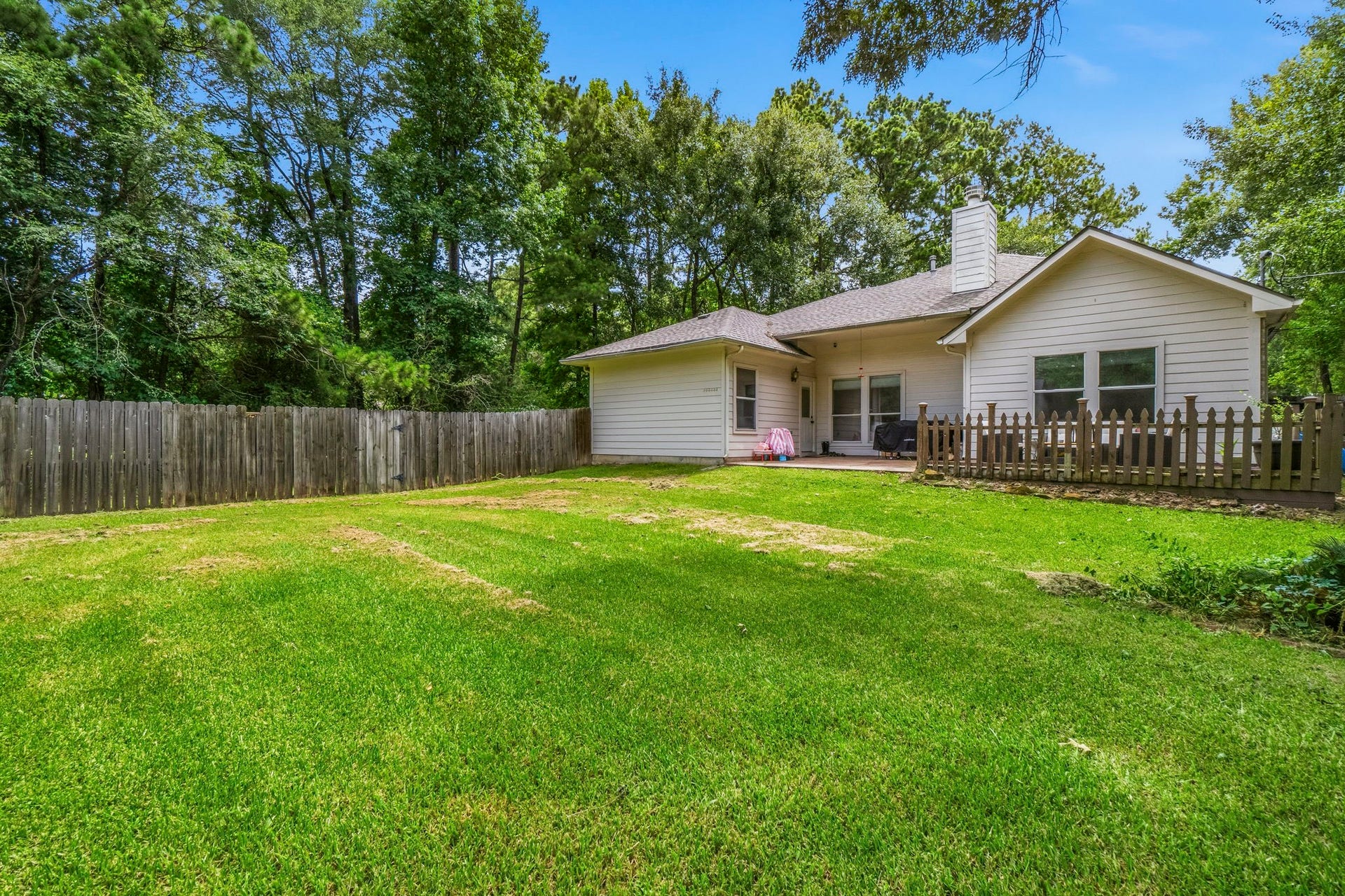 34019 Conroe Huffsmith Road, Magnolia, TX 77354 Charming single-story home with a spacious, fenced backyard surrounded by lush trees, offering privacy and a serene outdoor retreat.