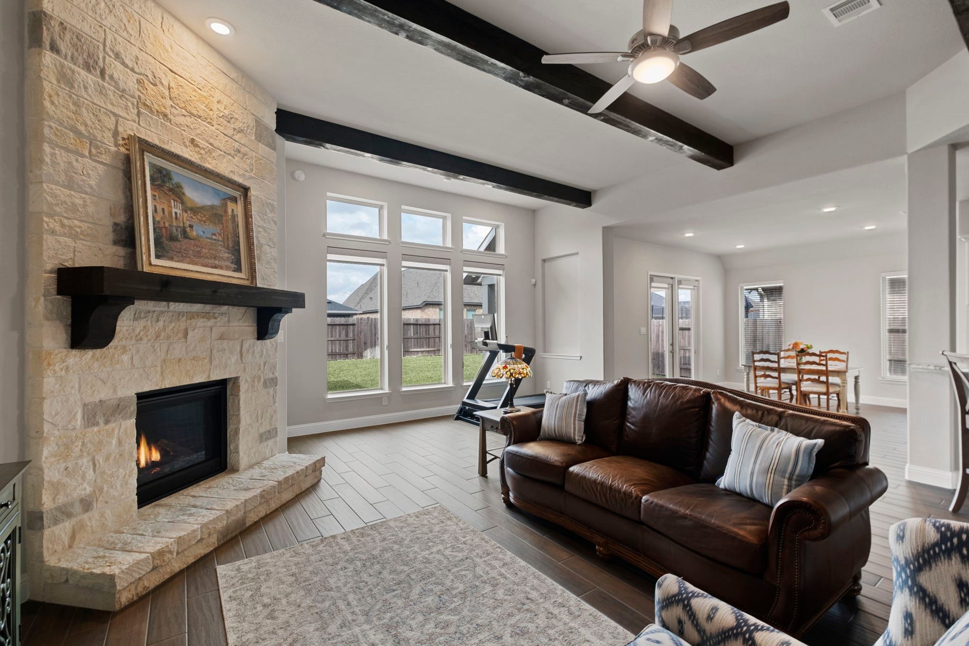 19314 Trotting Green Trail, Tomball, TX 77377 This inviting living room features a cozy stone fireplace, exposed wooden beams, and ample natural light from large windows. It seamlessly connects to the dining area and offers a comfortable, open feel, perfect for gatherings.