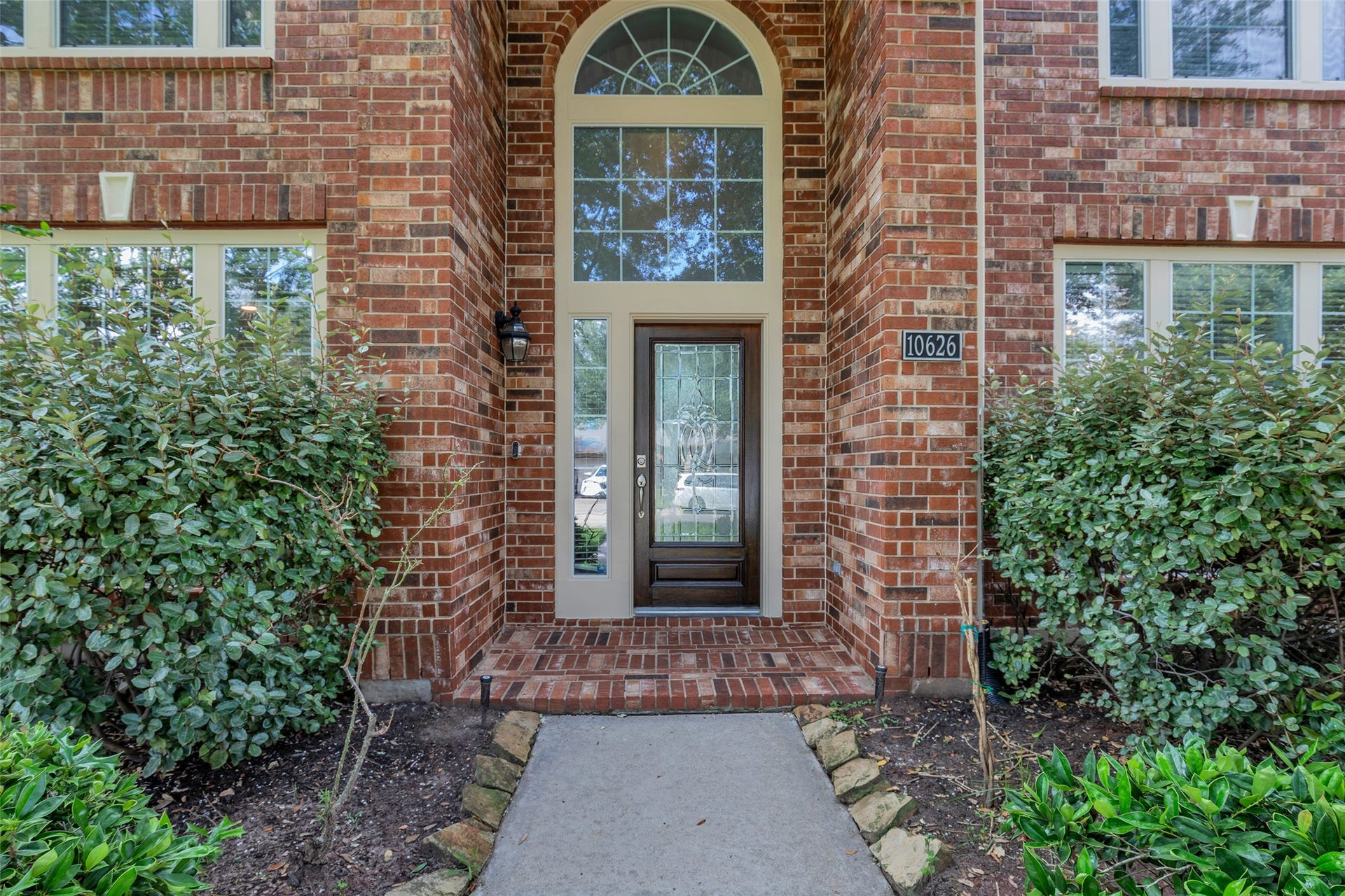 10626 Cortland Ridge Lane, Cypress, TX 77433 Brick entrance with a grand arched window and elegant glass door, framed by manicured greenery.
