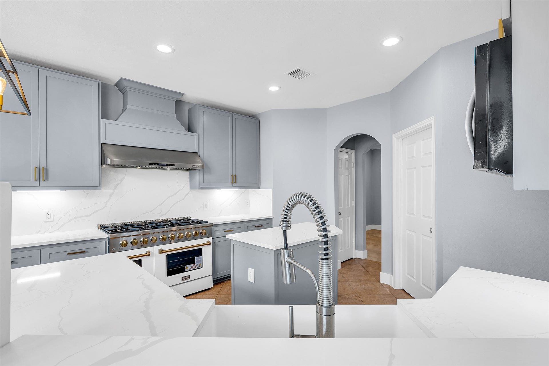 10626 Cortland Ridge Lane, Cypress, TX 77433 Modern kitchen with sleek gray cabinetry, a professional-grade 48 inch range, and elegant quartz countertops, complemented by a high-arc faucet and bright recessed lighting.