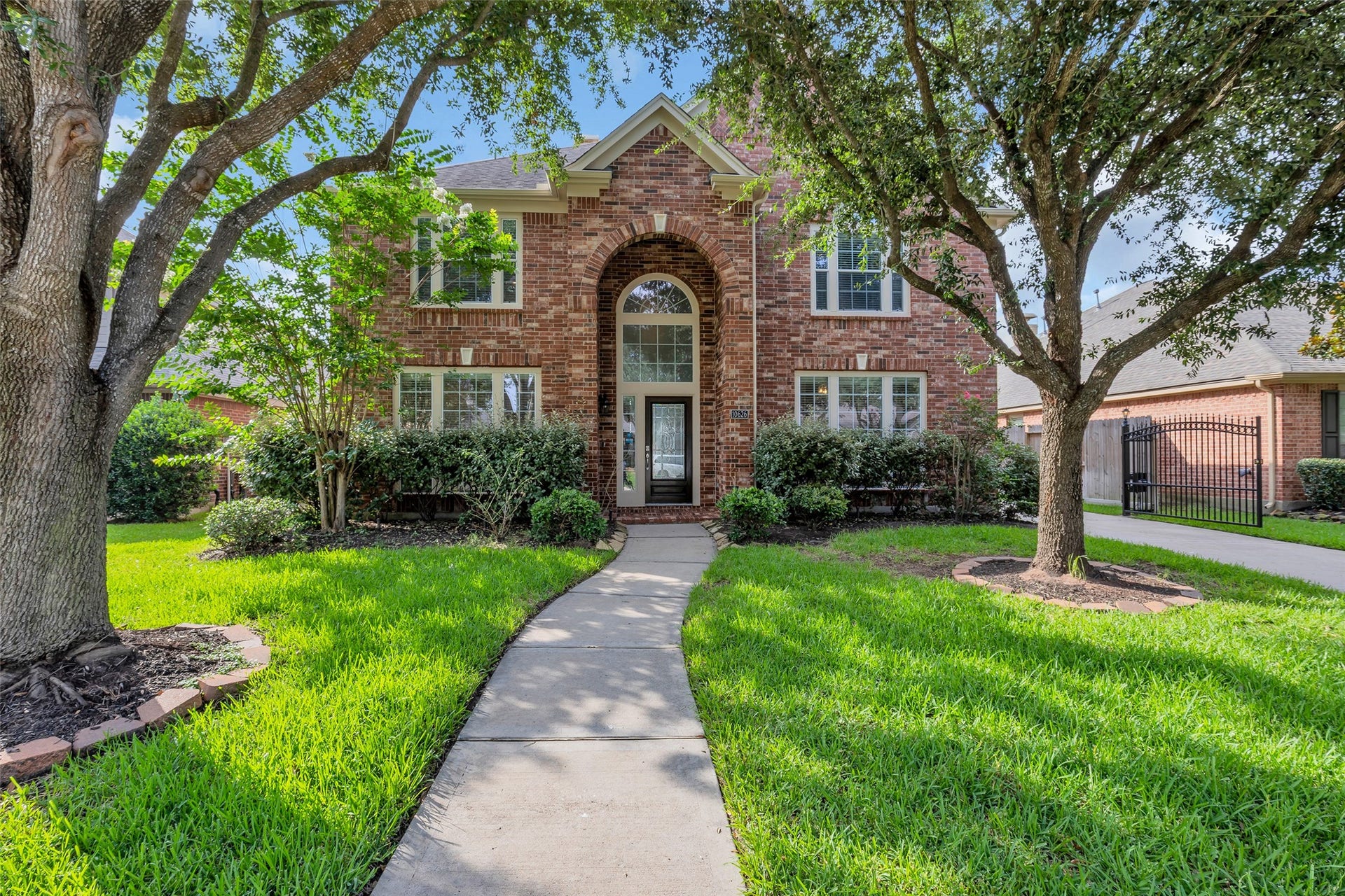 10626 Cortland Ridge Lane, Cypress, TX 77433 Charming two-story brick home with a grand arched entryway, framed by mature trees and lush landscaping, offering a welcoming and serene curb appeal.