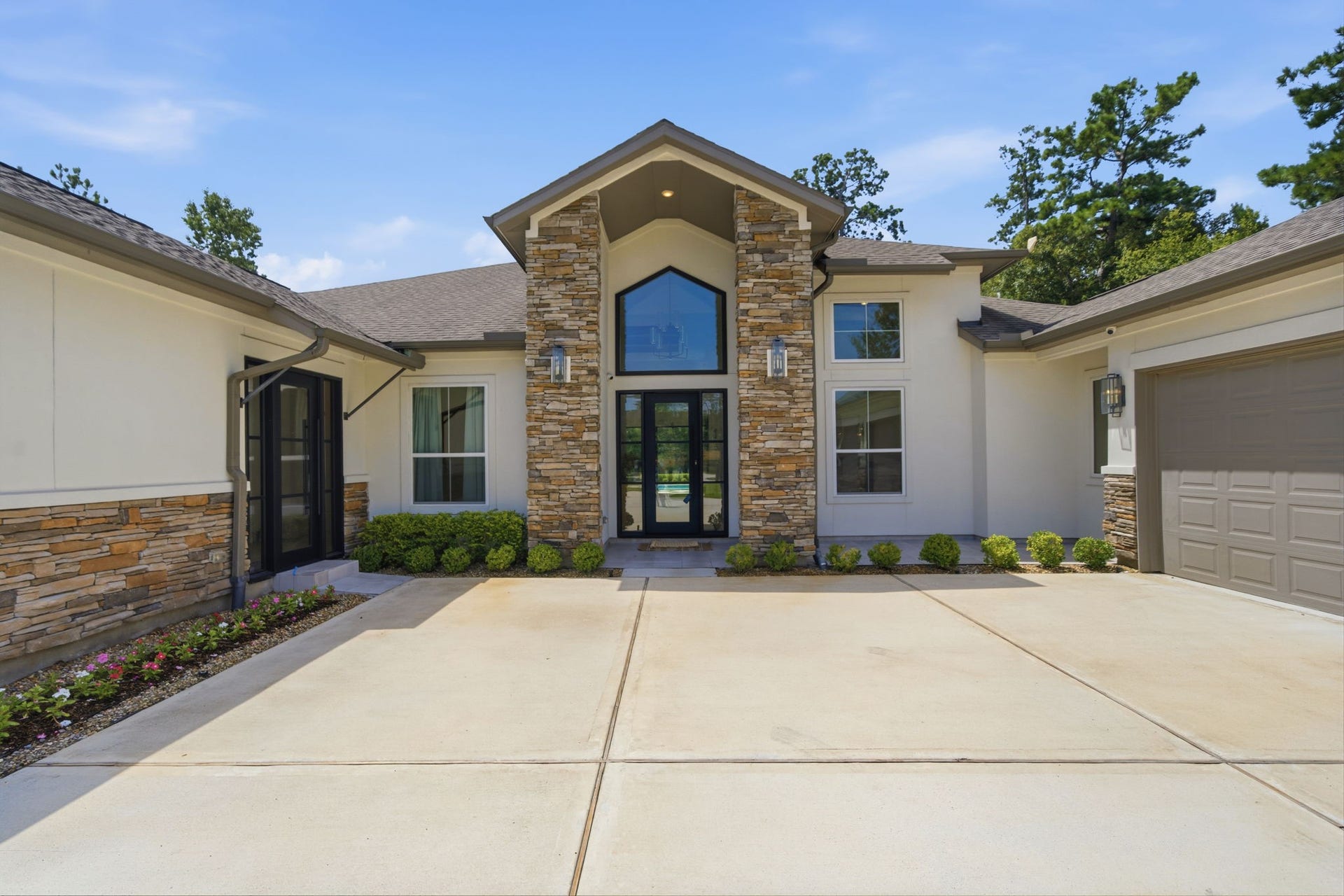 6310 Star Light Court, Spring, TX 77386 Stunning modern home with a grand entrance, featuring a striking stone faade and expansive driveway, set against a backdrop of lush greenery.