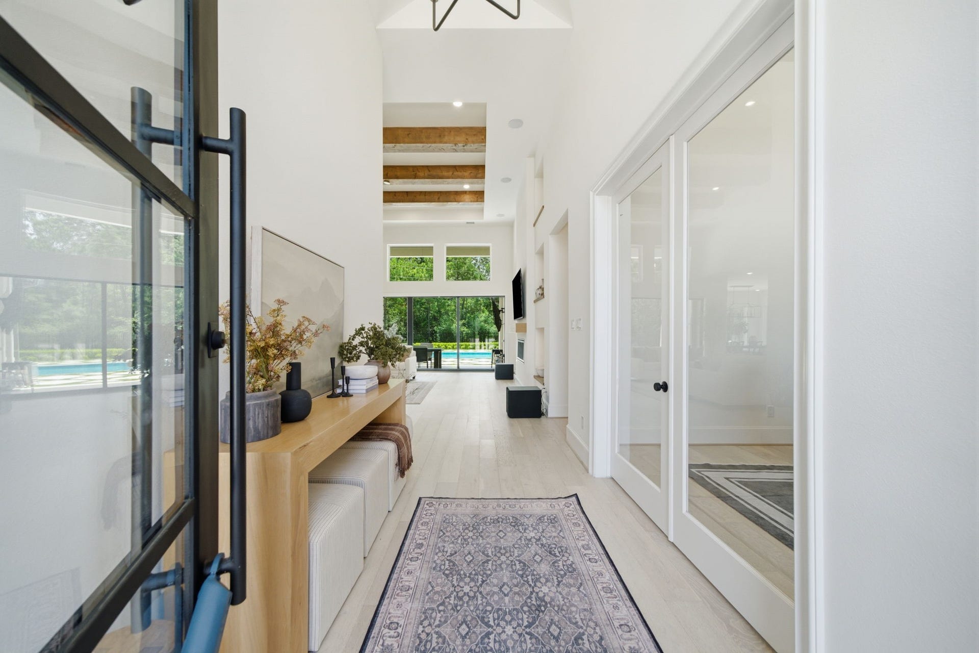 6310 Star Light Court, Spring, TX 77386 Elegant entryway with high ceilings, exposed beams, and abundant natural light leading to a view of the garden and pool area.