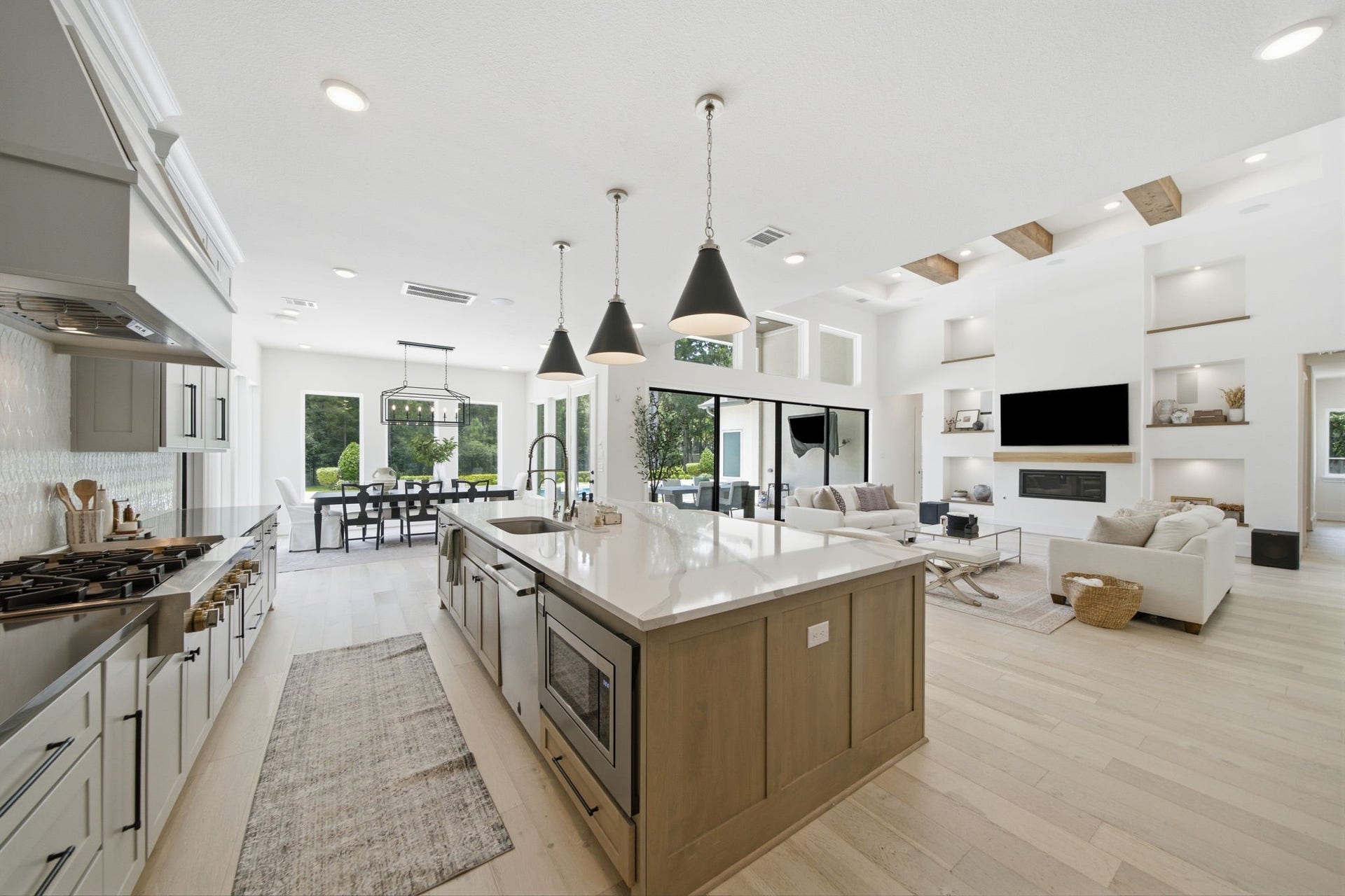 6310 Star Light Court, Spring, TX 77386 Spacious open-concept living area featuring a modern kitchen with a large island, elegant pendant lighting, and sleek cabinetry, seamlessly flowing into a bright dining space and cozy living room with built-in shelving and a stylish fireplace.