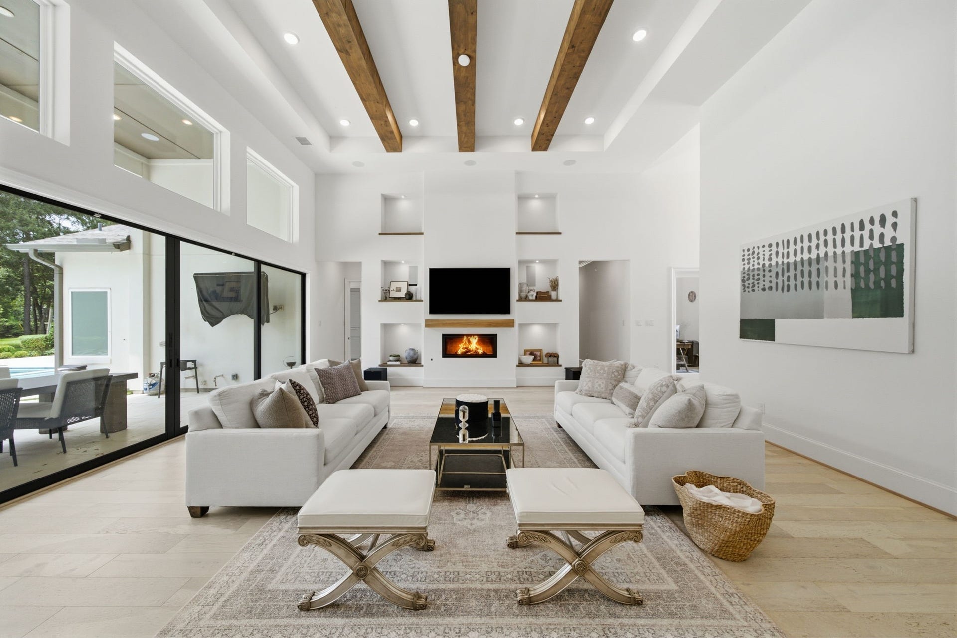 6310 Star Light Court, Spring, TX 77386 Stunning living room with high ceilings, exposed wooden beams, and abundant natural light from floor-to-ceiling windows. Features a modern fireplace, sleek built-in shelving, and an open view to the patio and pool area, perfect for entertaining.