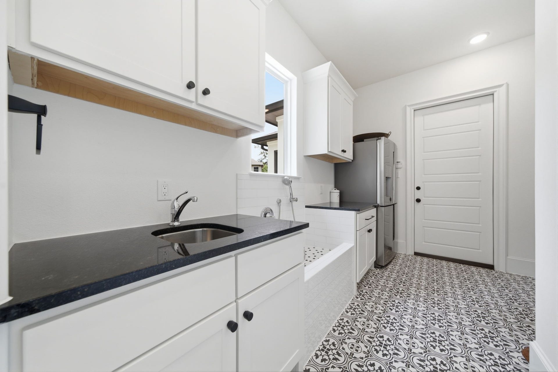 6310 Star Light Court, Spring, TX 77386 Stylish laundry room featuring elegant black countertops, crisp white cabinetry, and eye-catching patterned floor tiles, offering both functionality and charm.