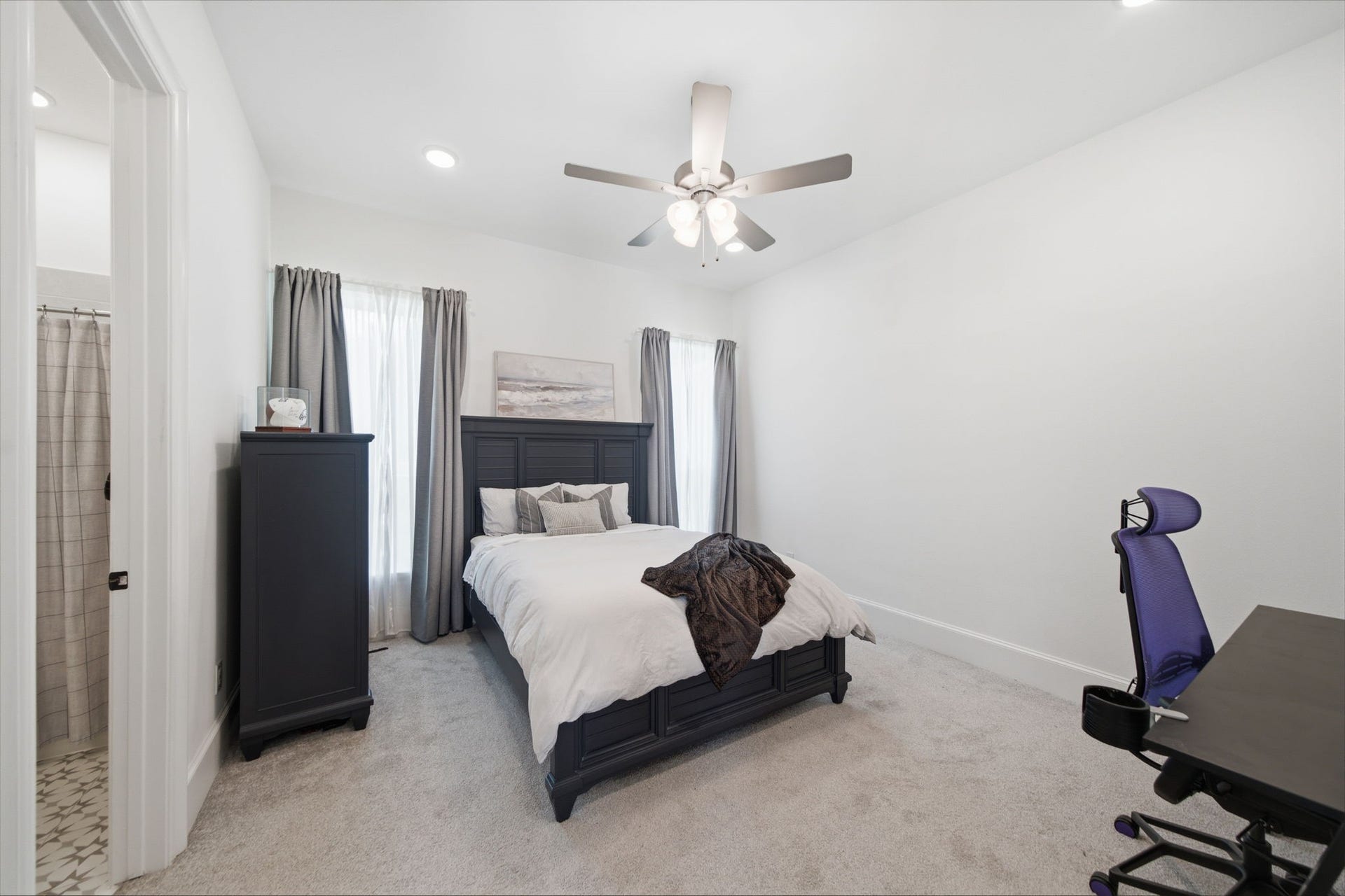 6310 Star Light Court, Spring, TX 77386 Spacious bedroom with cozy carpeting, featuring a stylish dark wood bed frame and matching furniture. Abundant natural light streams through the large windows, while a ceiling fan adds comfort. Adjacent en-suite bathroom enhances convenience.