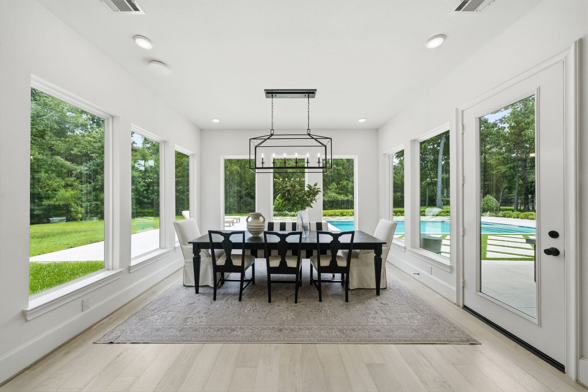 6310 Star Light Court, Spring, TX 77386 Bright and airy dining area with large windows showcasing a lush garden and sparkling pool view, featuring elegant lighting and a spacious table for gatherings.