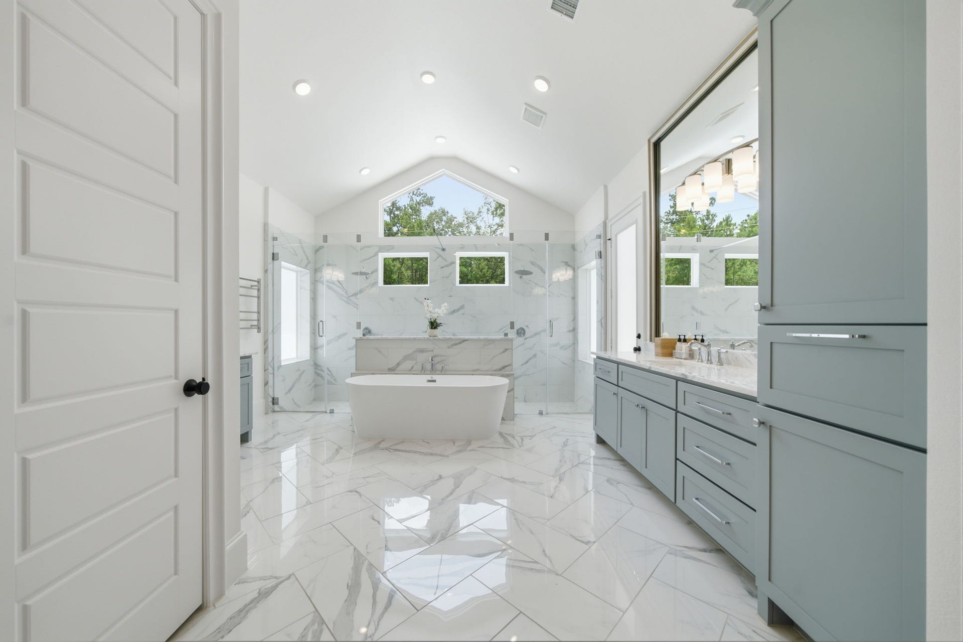 6310 Star Light Court, Spring, TX 77386 Luxurious bathroom featuring a freestanding tub, sleek marble flooring, and dual vanities. The vaulted ceiling and large windows provide abundant natural light.