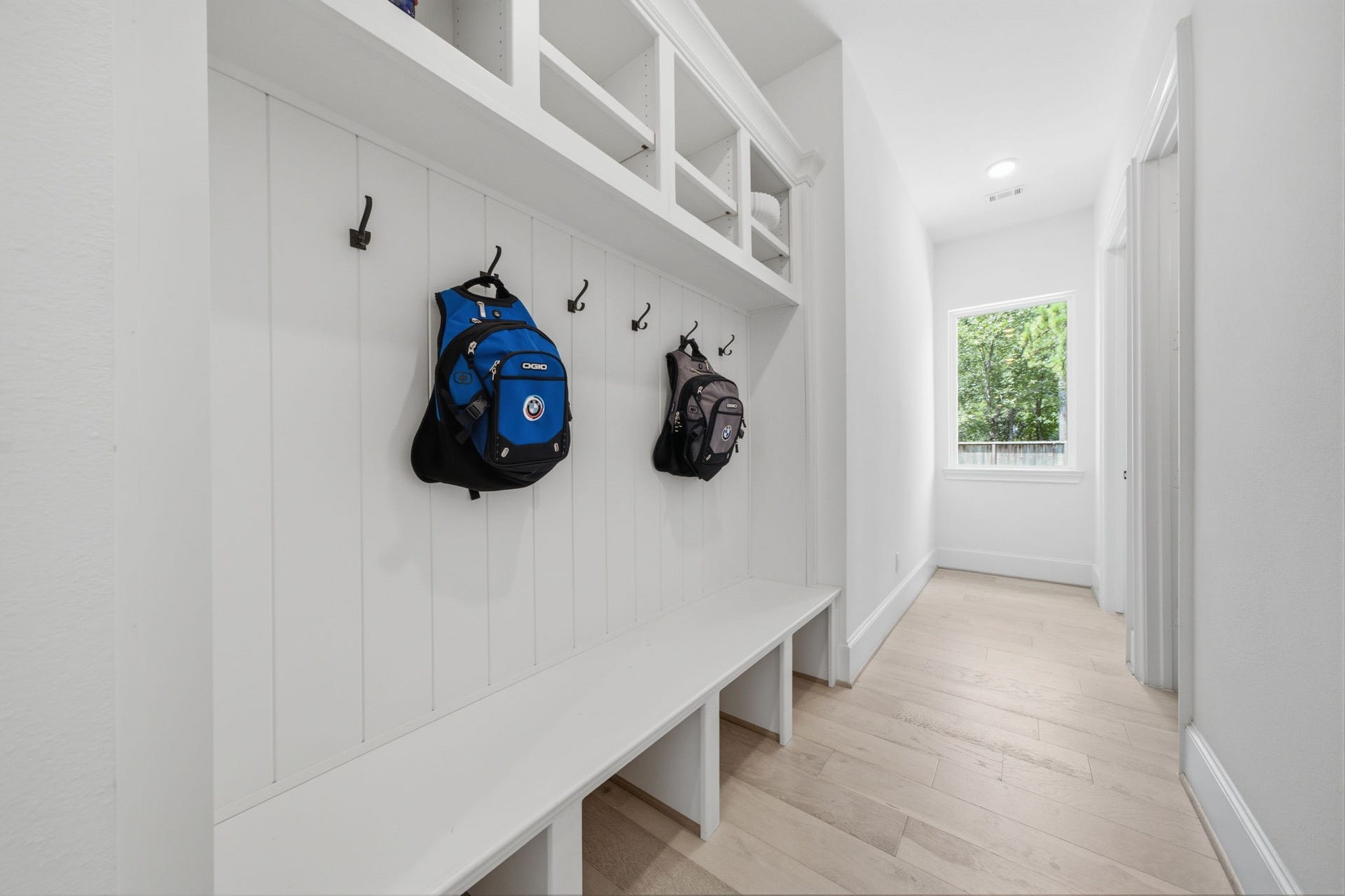 6310 Star Light Court, Spring, TX 77386 Spacious mudroom featuring built-in storage with hooks and cubbies, complemented by sleek white paneling and light wood flooring, offering a practical and stylish entry solution.