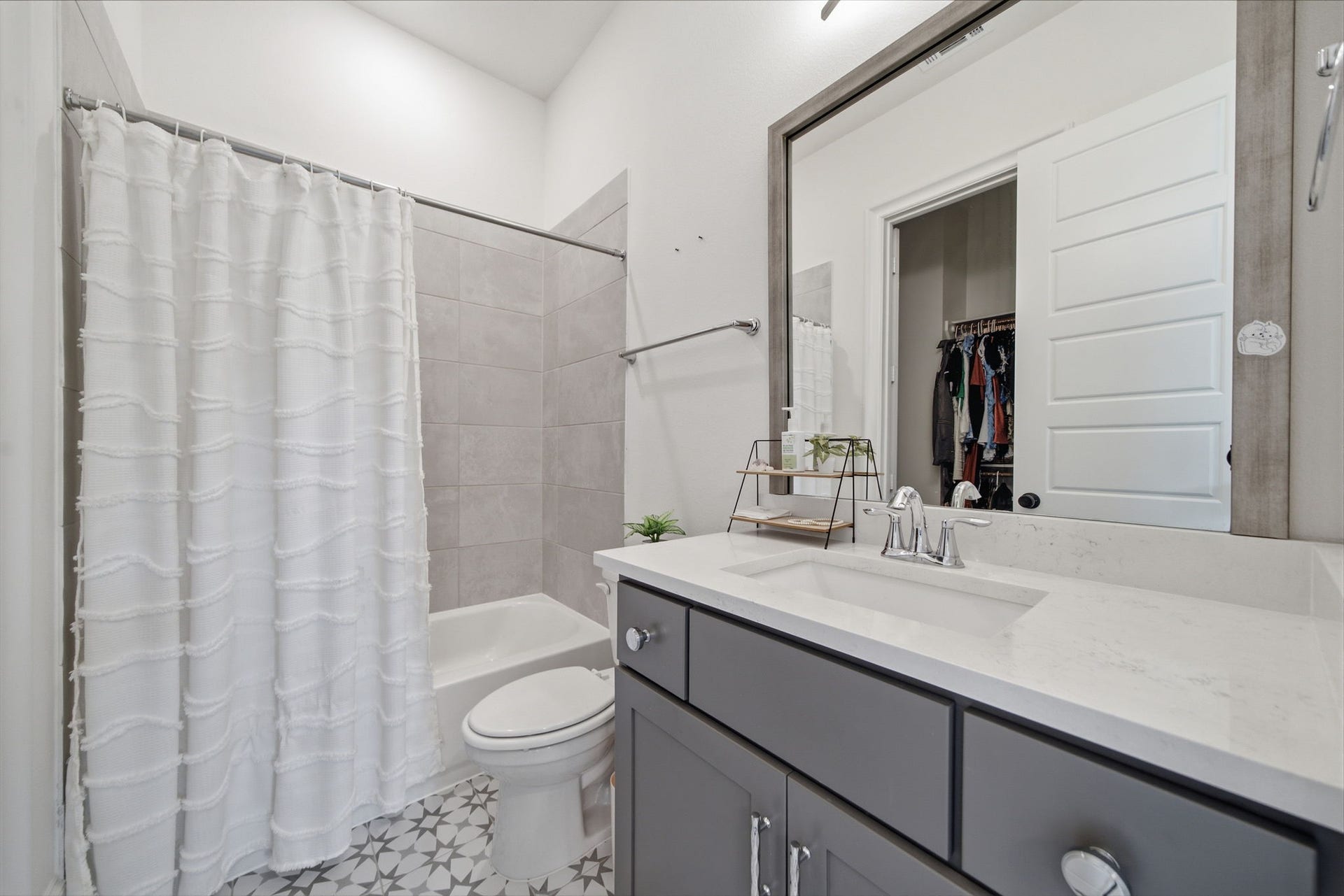 6310 Star Light Court, Spring, TX 77386 Modern bathroom featuring sleek gray cabinetry, a spacious mirror, and a stylish vanity with a polished countertop. The shower-tub combo is complemented by elegant tile work and a bright curtain, creating a fresh and inviting space.
