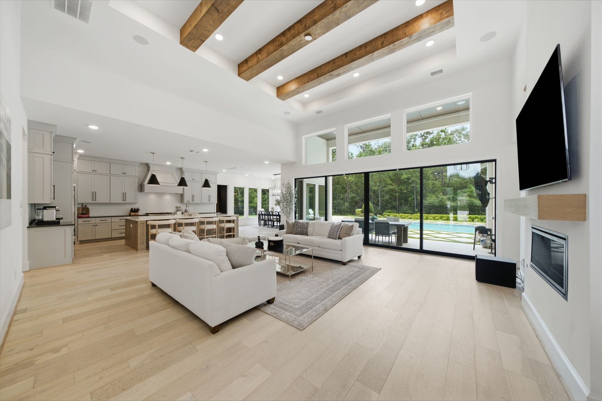 6310 Star Light Court, Spring, TX 77386 Stunning open-concept living area with high ceilings, exposed wooden beams, and expansive glass doors leading to a serene outdoor space.