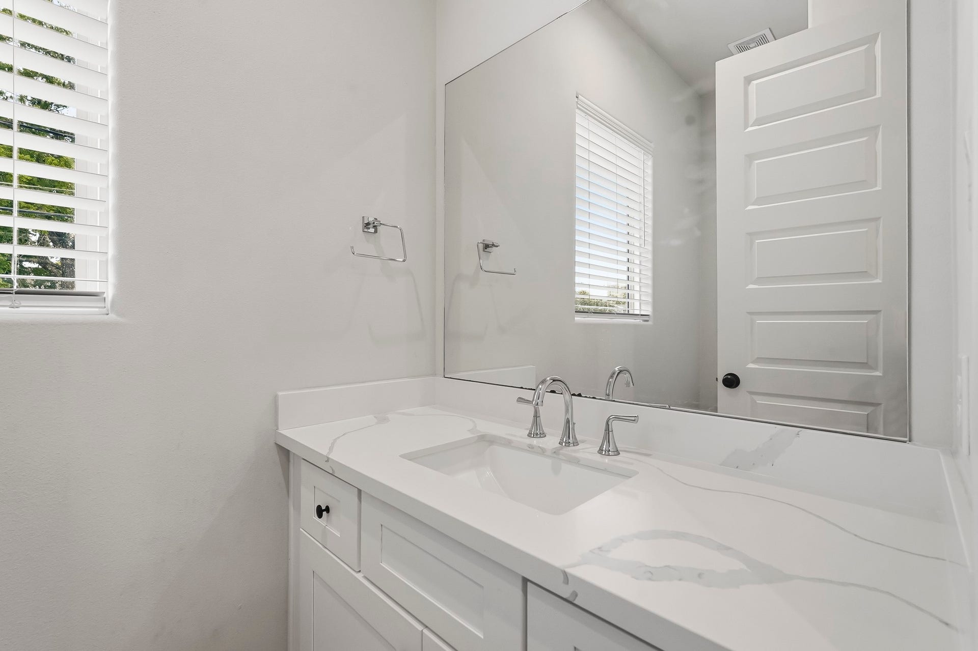 3109 Arlington Street, Houston, TX 77018 Bright and modern half bath featuring a white vanity with a marble-inspired quartz countertop, undermount sink, and polished chrome fixtures. A large wall mirror enhances the sense of space, while the window with faux-wood blinds brings in plenty of natural light.