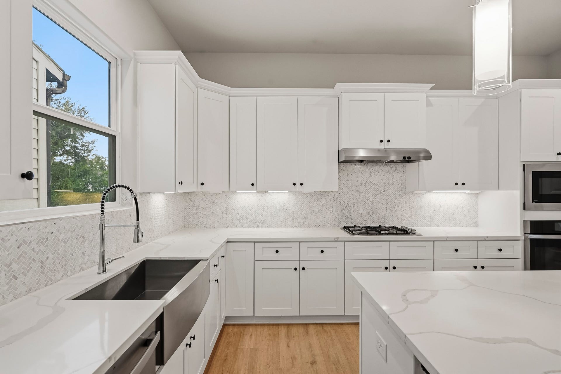 3109 Arlington Street, Houston, TX 77018 A textured tile backsplash, under-cabinet lighting, and contemporary pendant lights add style, while luxury vinyl plank flooring provides a welcoming contrast to the clean white finishes.