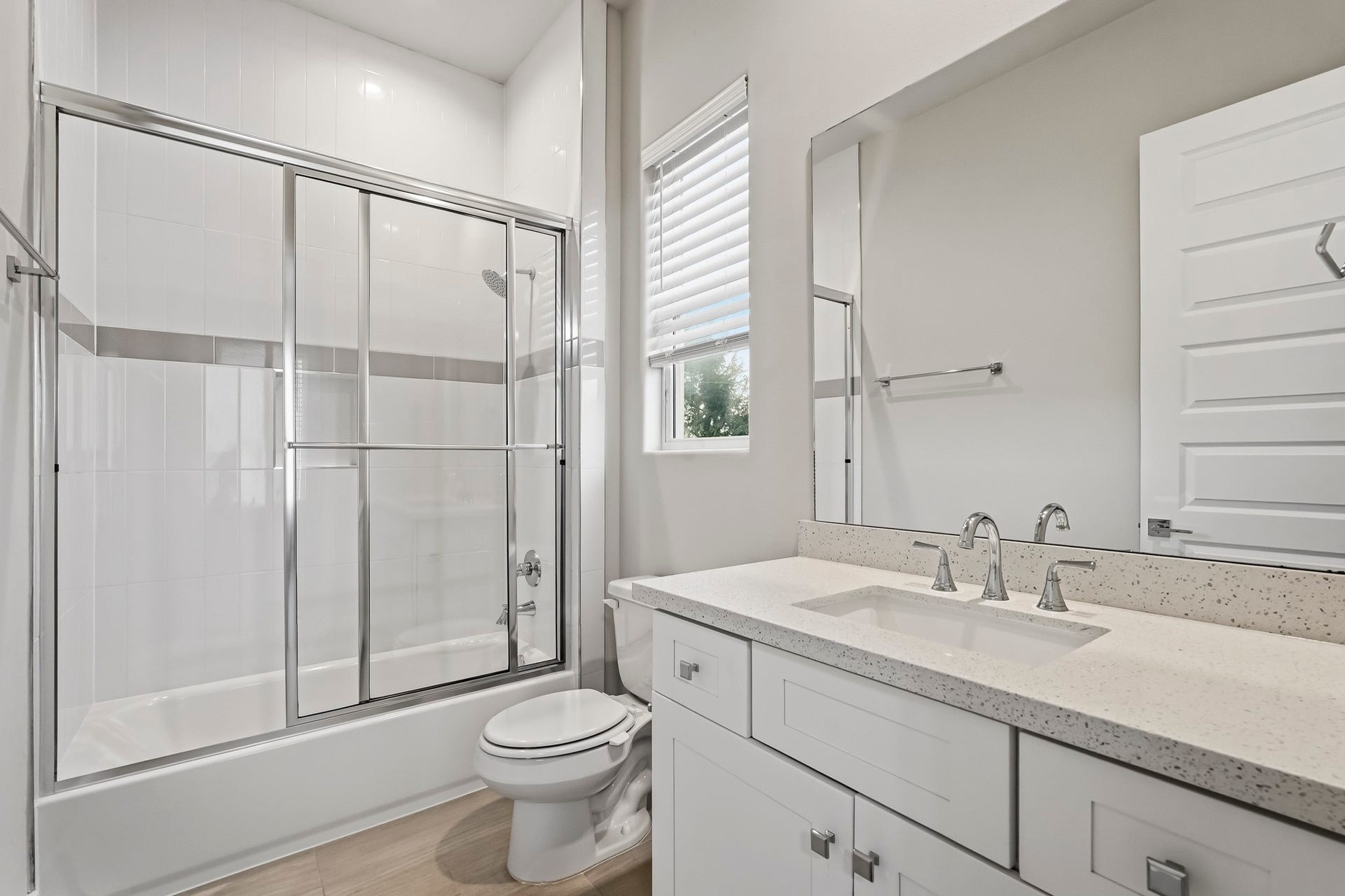 3109 Arlington Street, Houston, TX 77018 Bright and modern full bathroom featuring a tub-and-shower combination with a glass sliding enclosure, crisp white tile surround, and a sleek horizontal accent. The white vanity offers generous counter and storage space with a light quartz countertop, undermount sink, and polished chrome fixtures.