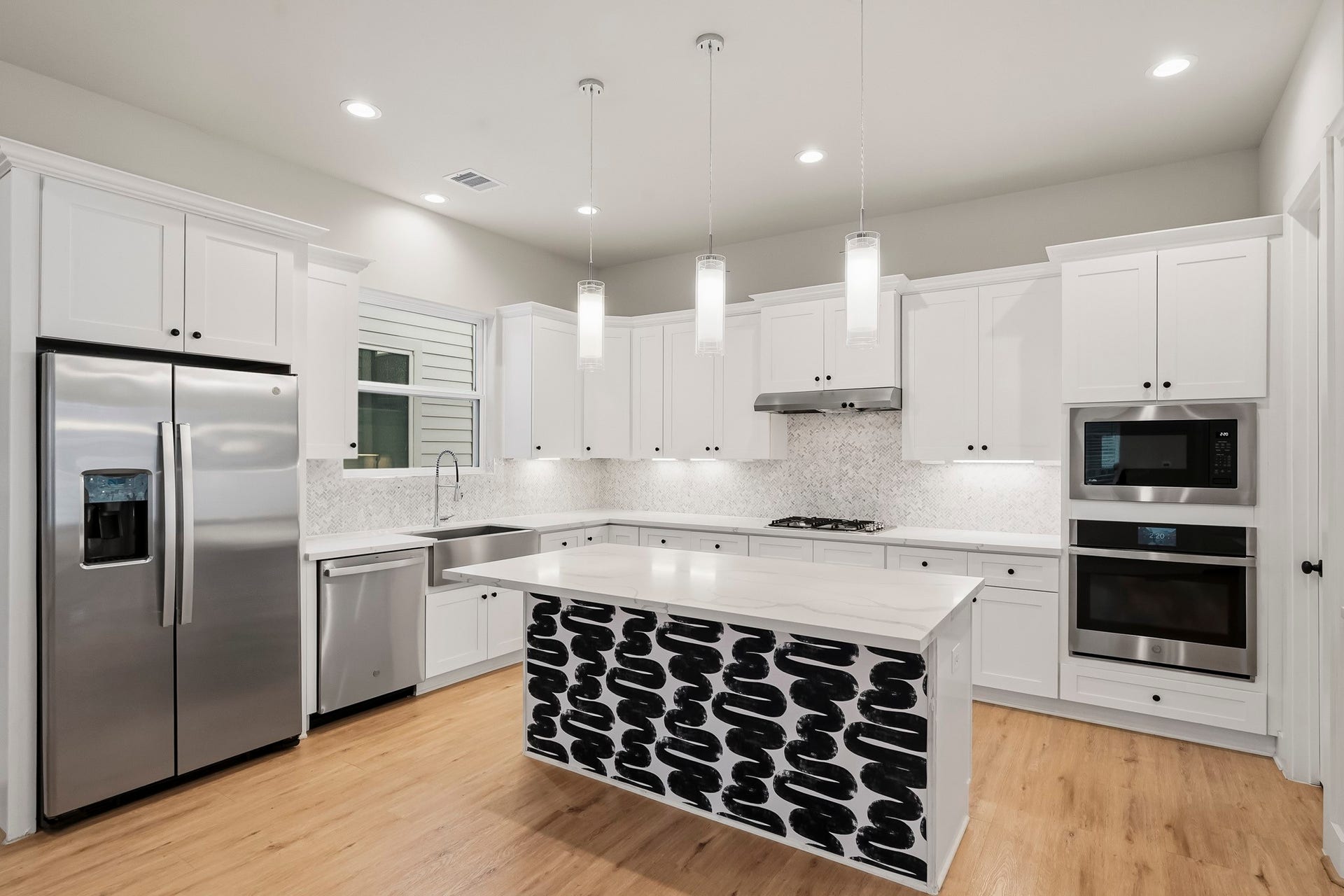 3109 Arlington Street, Houston, TX 77018 Bright, modern kitchen featuring crisp white cabinetry, quartz-style countertops, and a spacious center island accented with a bold black-and-white design. Stainless steel appliances include a refrigerator, dishwasher, gas cooktop, built-in microwave, and oven.