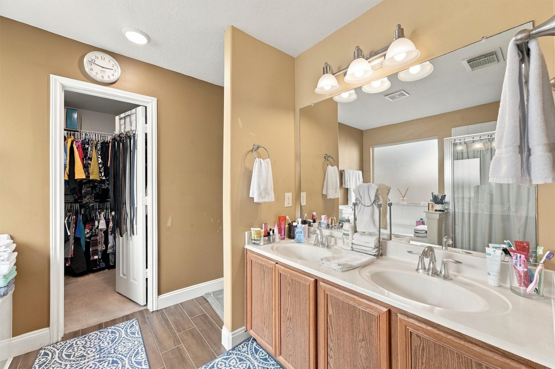 18931 Bonners Park Circle, Katy, TX 77449 Elegant bathroom featuring a double vanity with ample counter space, warm lighting, and a large mirror. Attached is a spacious walk-in closet, offering plenty of storage.