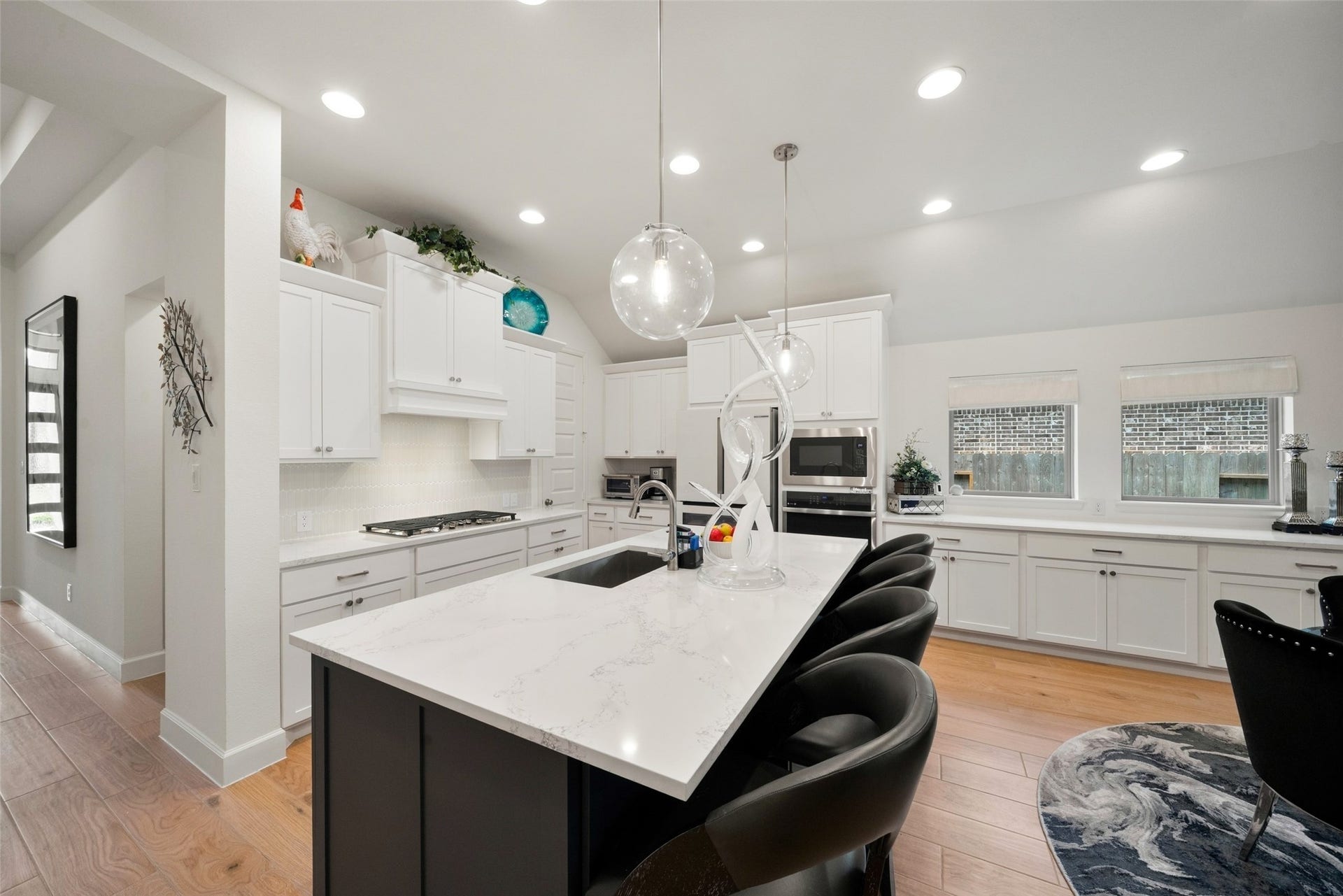 118 Sierra Stream Court, Conroe, TX 77304 Sophisticated kitchen showcases an oversized island with generous seating, extensive white cabinetry, stainless steel appliances, and an elegant tile backsplash. Additional cabinetry and countertop space beneath the windows provide exceptional storage and functionality.