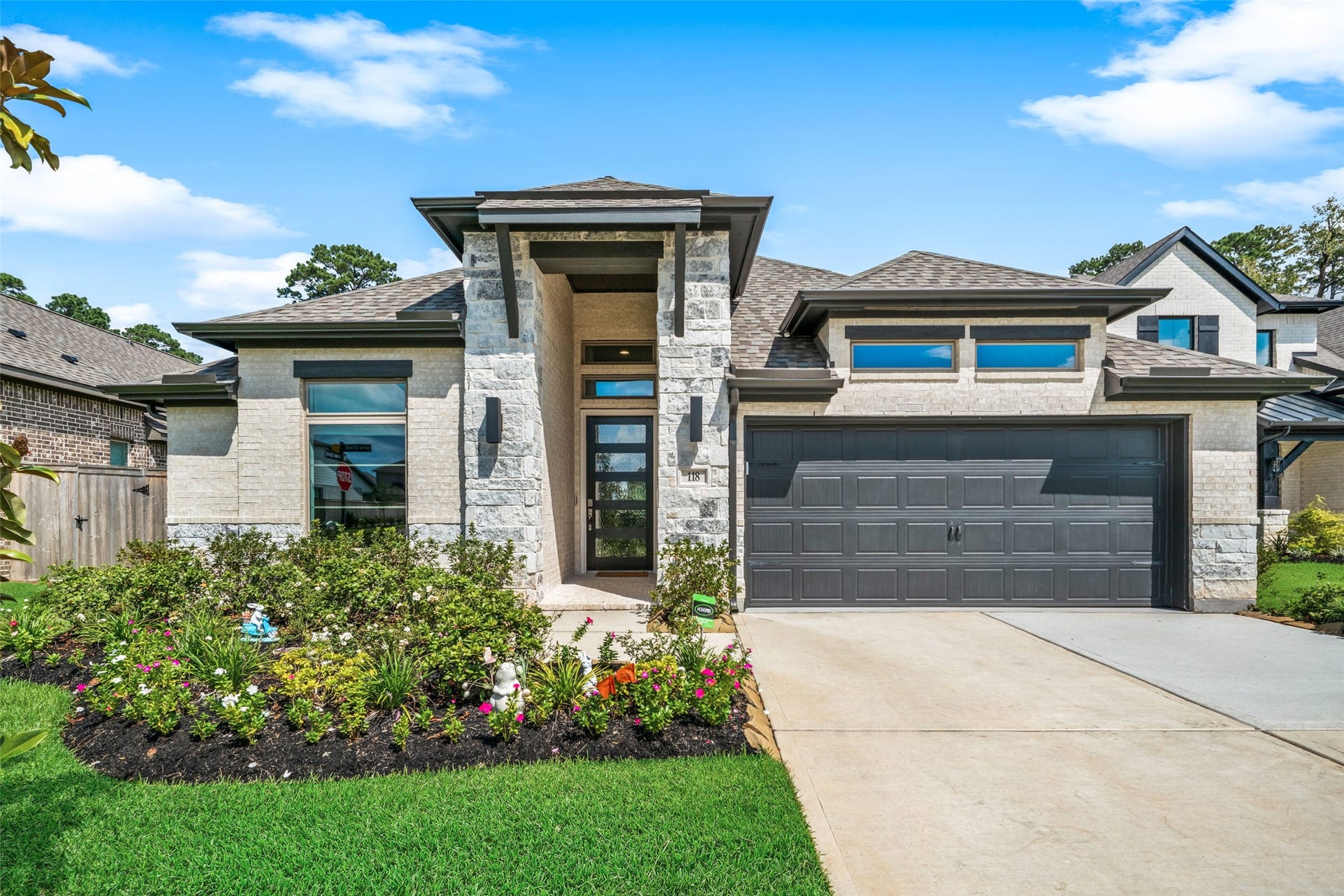118 Sierra Stream Court, Conroe, TX 77304 Elegant stonework, expansive windows, and a dramatic recessed entry create a distinctive first impression. Lush flower beds and mature landscaping add warmth and charm to the home's modern design.