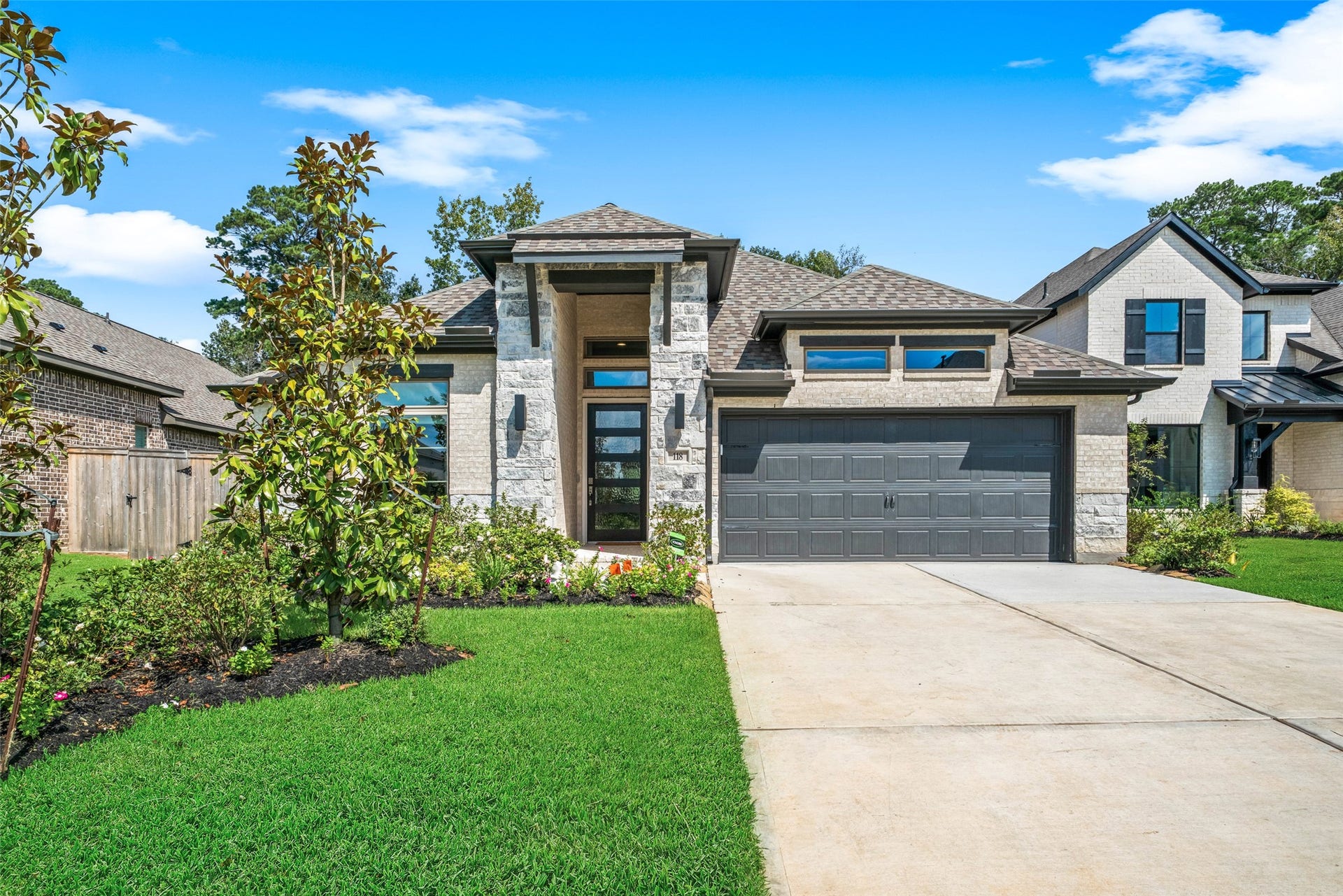 118 Sierra Stream Court, Conroe, TX 77304 Impressive front elevation showcases a soaring covered entry, sleek black accents, and thoughtfully designed landscaping. A welcoming approach complements the home's sophisticated architectural style.
