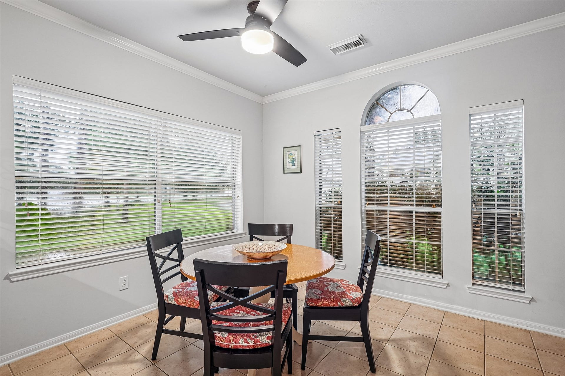 Bright dining area with large windows, tile flooring, and a ceiling fan, offering a cozy setting for meals.
