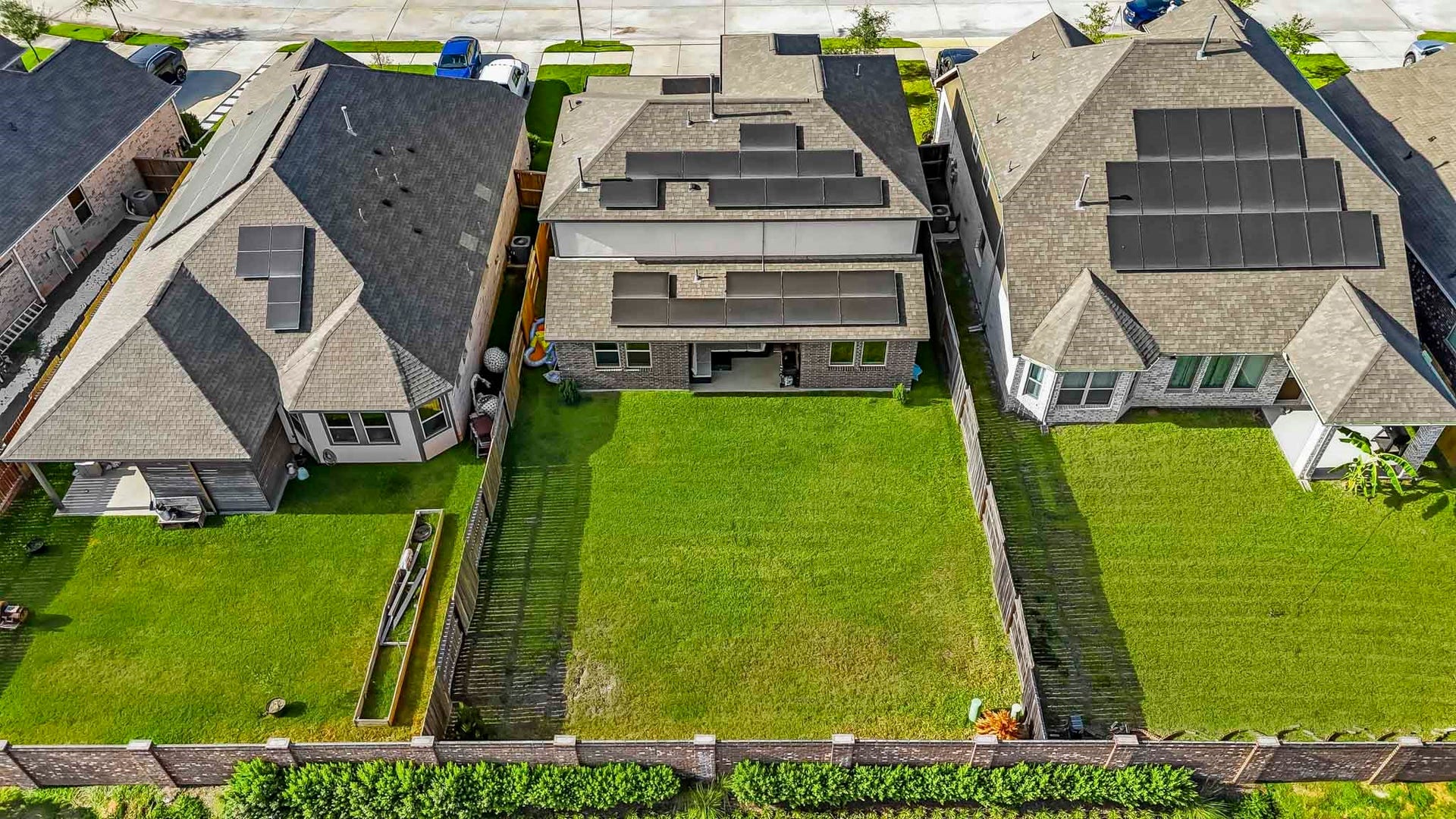 This aerial view showcases the homes spacious backyard and 6,351 sq. ft. lot, offering a generous stretch of fully fenced green space. The expansive lawn provides plenty of room for outdoor entertaining, recreation, a play area, or future landscaping possibilities, while the covered patio extends the homes living space outdoors. Solar panels can also be seen across the roof, adding an energy-efficient feature.