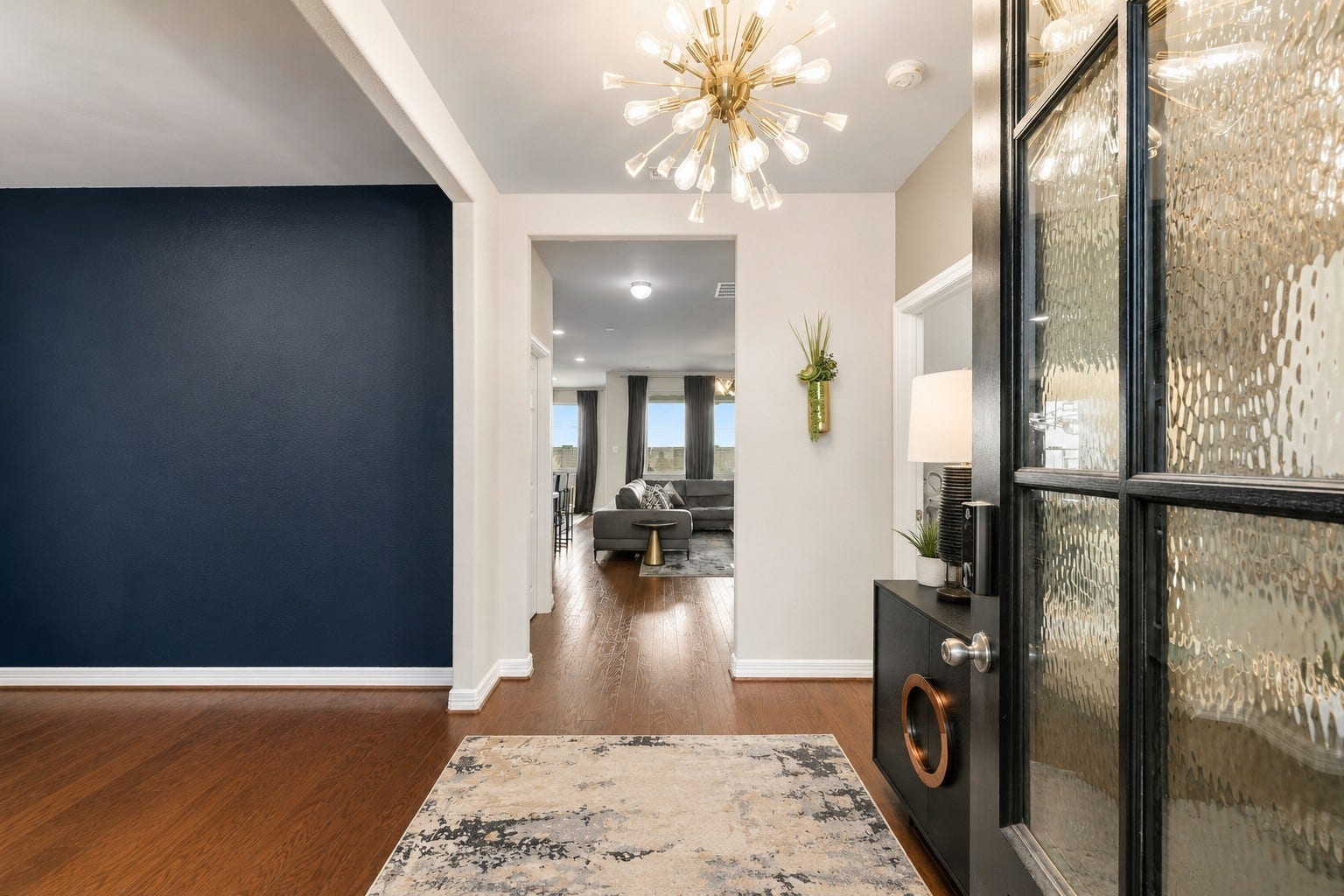 This welcoming entryway makes a stylish first impression with warm wood flooring, a dramatic statement chandelier, and a bold accent wall.