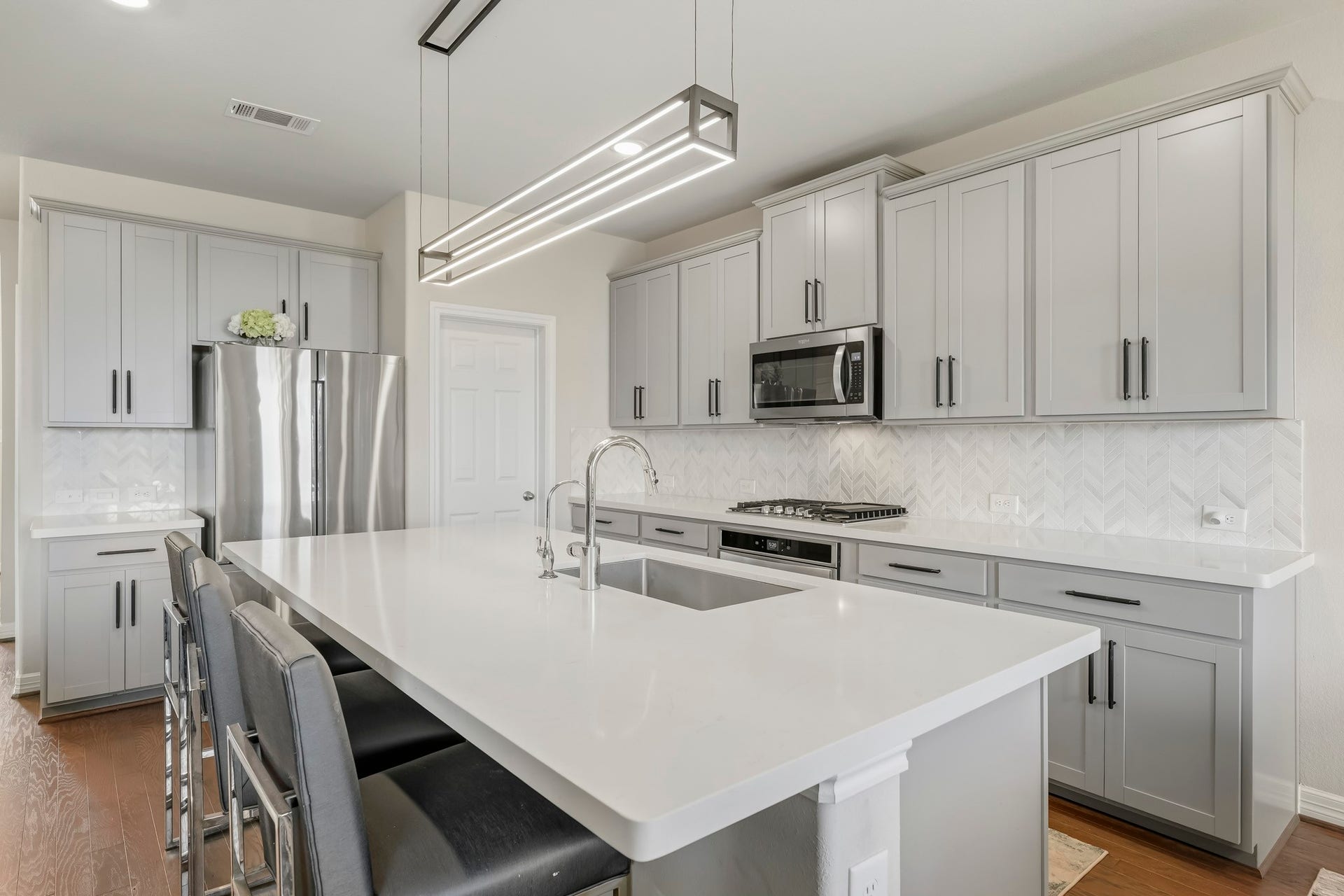 This beautifully updated kitchen features abundant cabinetry, sleek countertops, and a stylish herringbone tile backsplash. A large center island provides generous prep space, a built-in sink, and bar seating, making it ideal for everyday living and entertaining. Stainless steel appliances, a gas cooktop, modern fixtures, and contemporary lighting complete the bright, polished design.