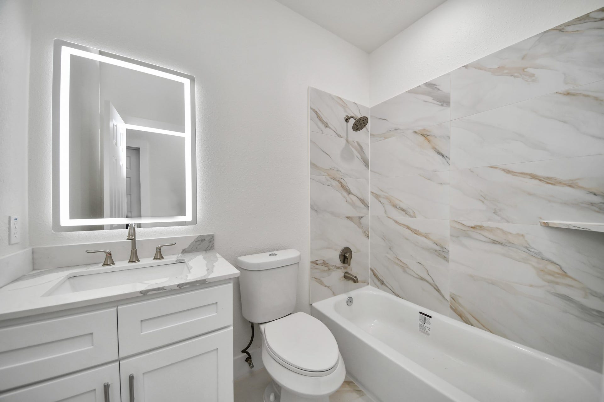 Elegant bathroom featuring a sleek vanity with a modern illuminated mirror, complemented by a luxurious bathtub and stylish marble-patterned tiles.