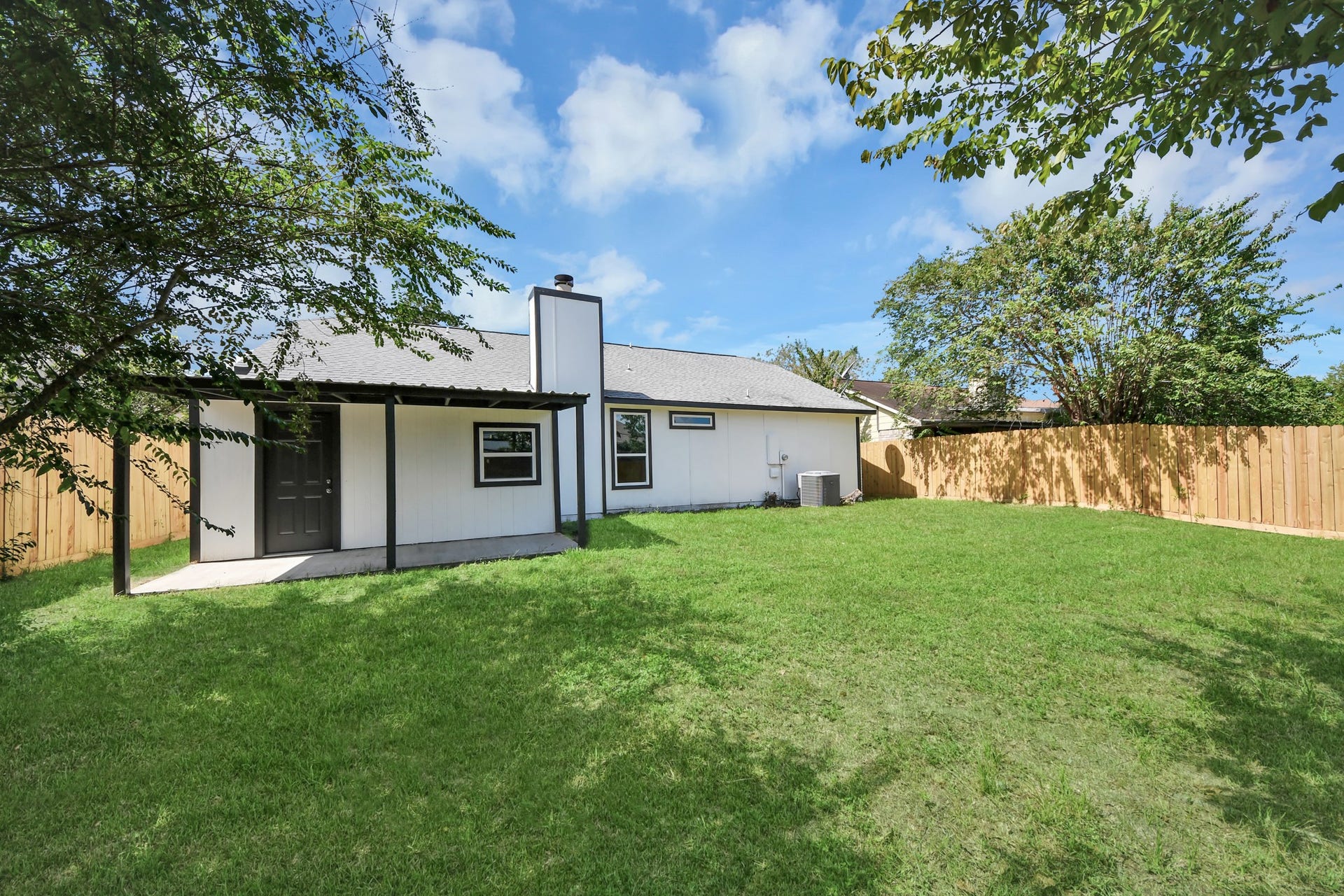 Charming home with a spacious backyard, lush green lawn, and a cozy covered patio perfect for relaxation.