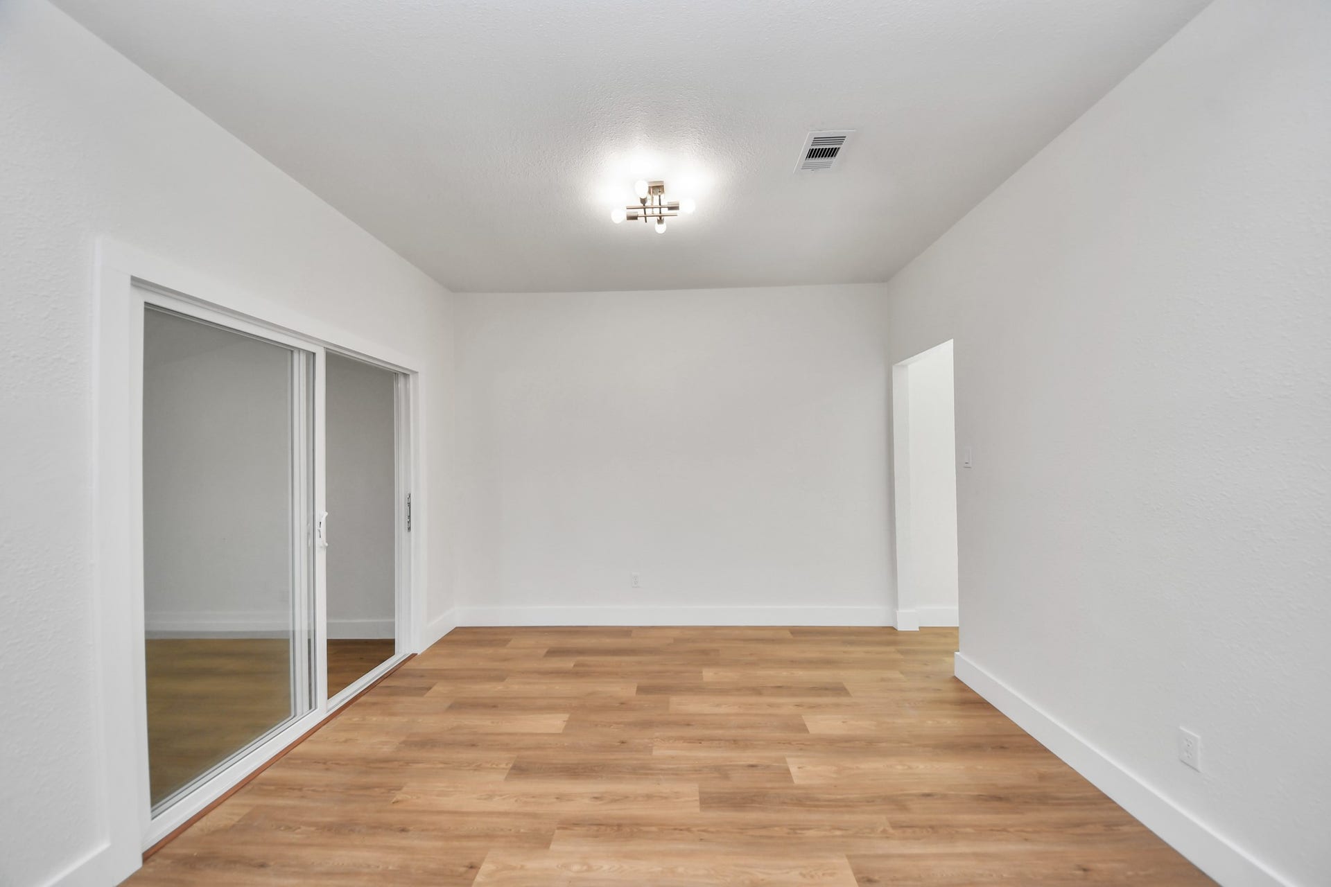 Spacious dinning room with sleek hardwood floors, modern lighting, and large sliding glass doors for ample natural light.