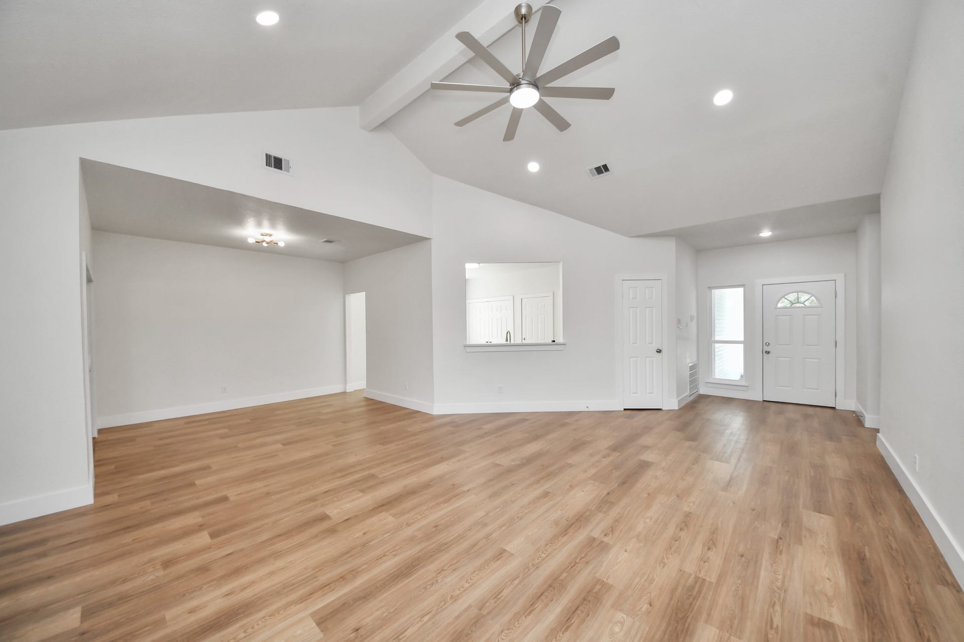 Spacious open-concept living area with elegant wood flooring, high vaulted ceilings, and a modern ceiling fan, offering a bright and inviting atmosphere.