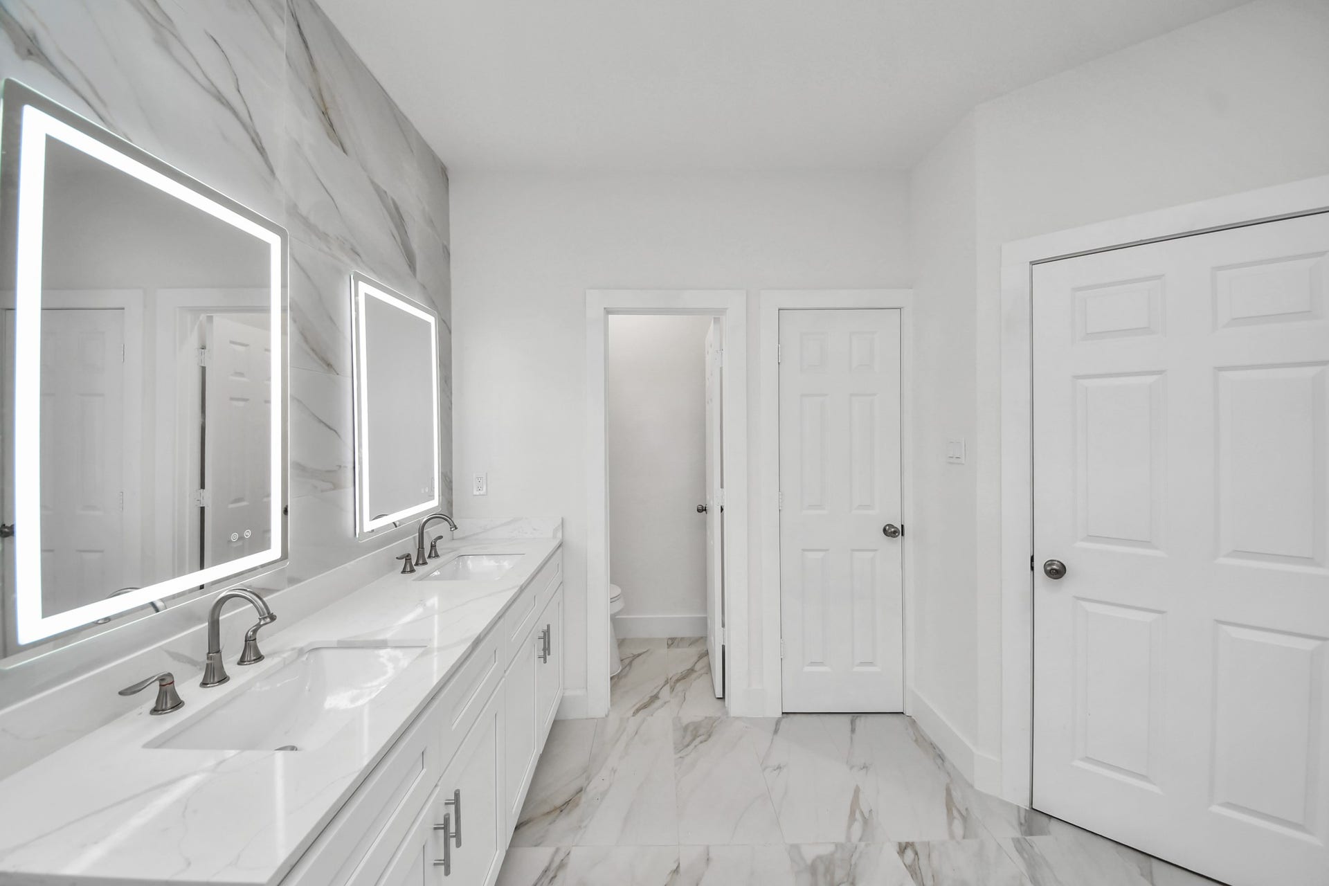 Luxurious bathroom featuring a double vanity with sleek marble countertops, modern backlit mirrors, and elegant fixtures, all complemented by a wall and polished Porcelin tile .