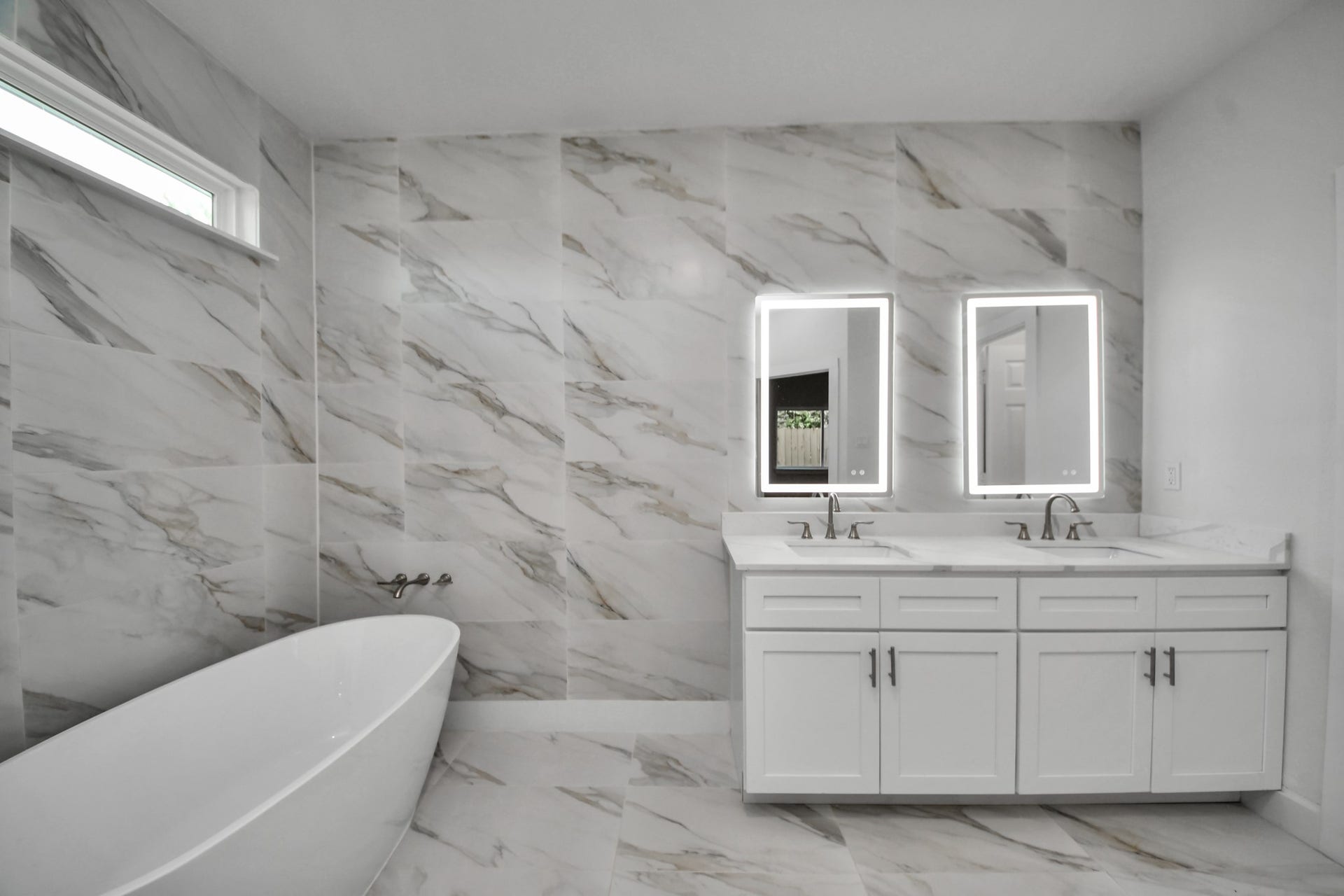 Luxurious bathroom featuring elegant marble tile, a modern freestanding tub, double vanity with illuminated mirrors, and sleek fixtures for a spa-like experience.