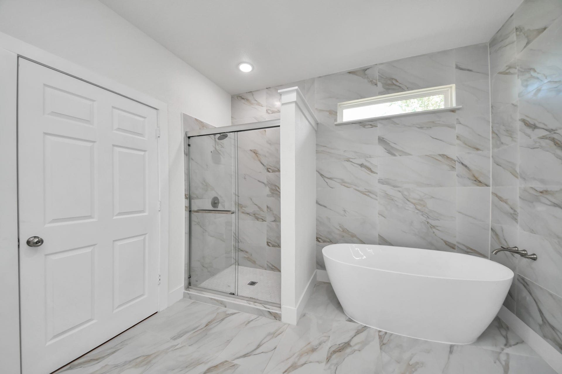 Elegant bathroom featuring a luxurious freestanding tub and a glass-enclosed shower, accented with stylish marble tile and modern fixtures.