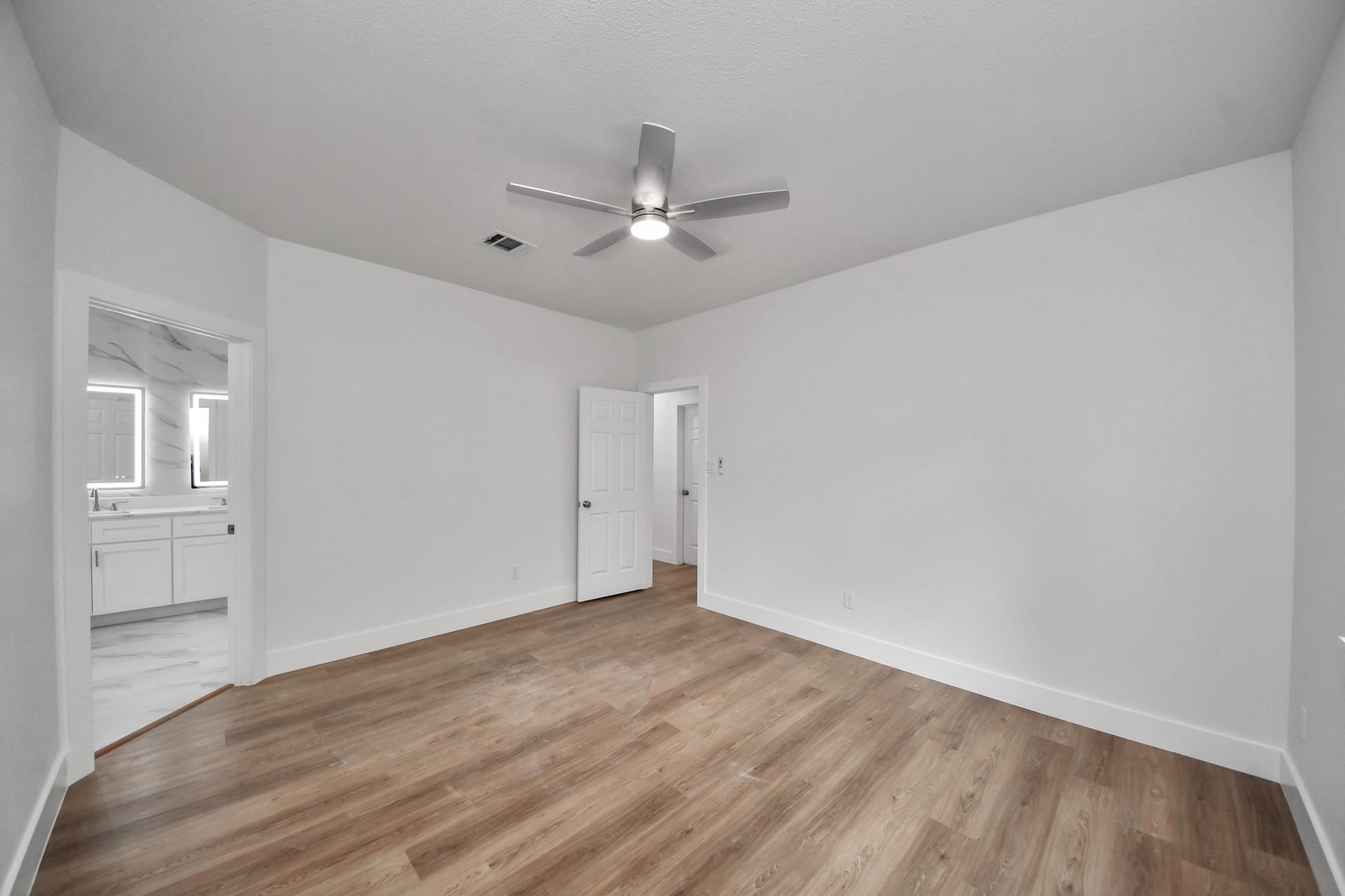 Spacious bedroom with sleek wood flooring, ceiling fan, and direct access to a modern en-suite bathroom.