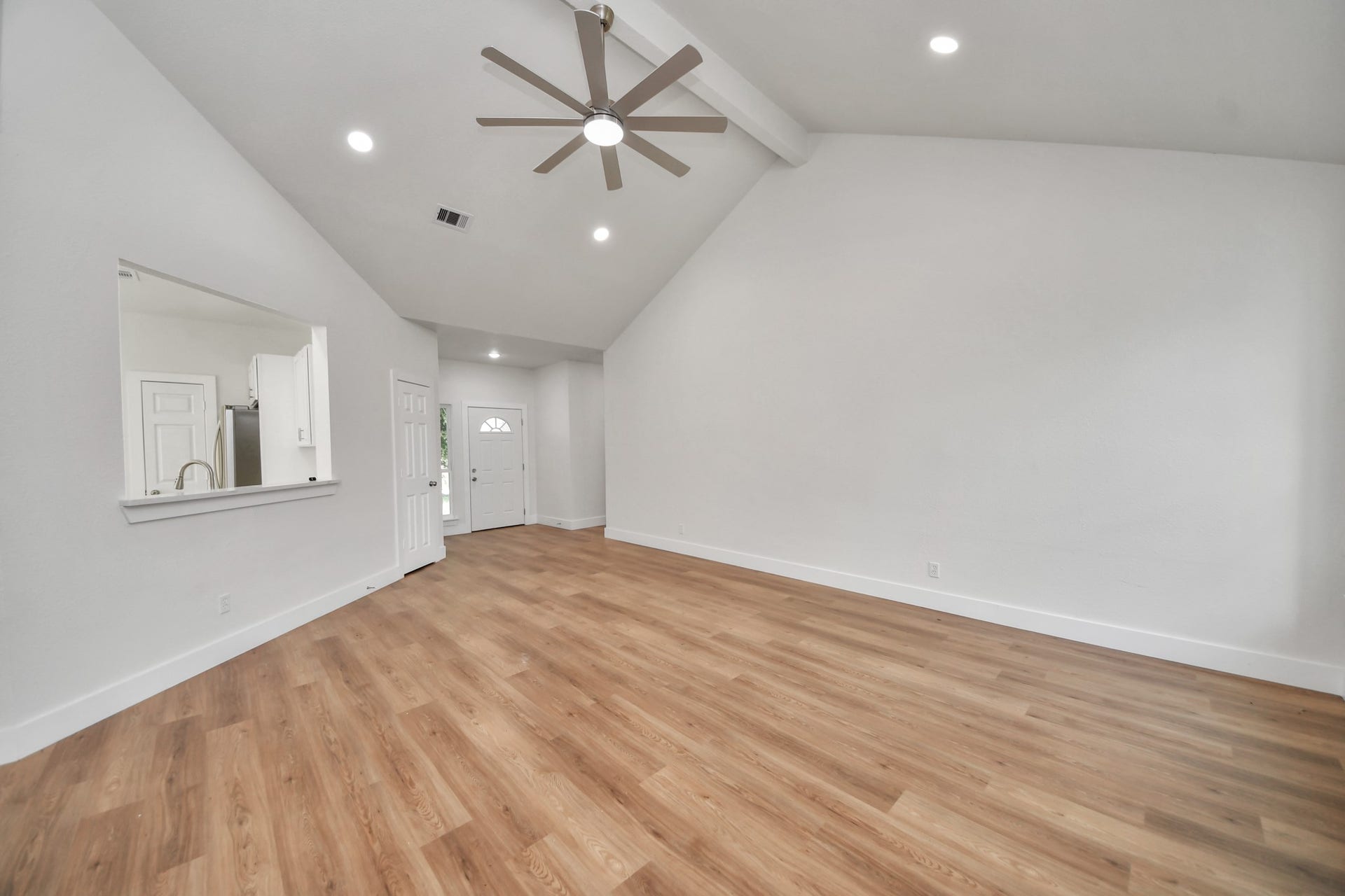 Spacious living area with vaulted ceilings, sleek ceiling fan, and elegant wood flooring, offering a bright and inviting atmosphere.