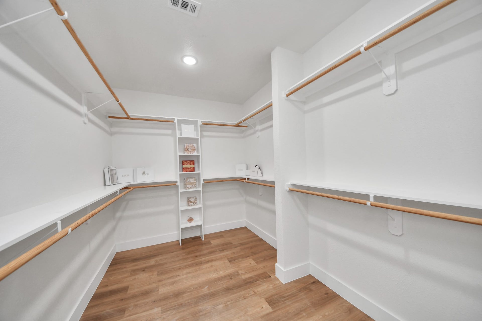Spacious walk-in closet with ample shelving and hanging space, complemented by sleek hardwood floors and bright lighting.