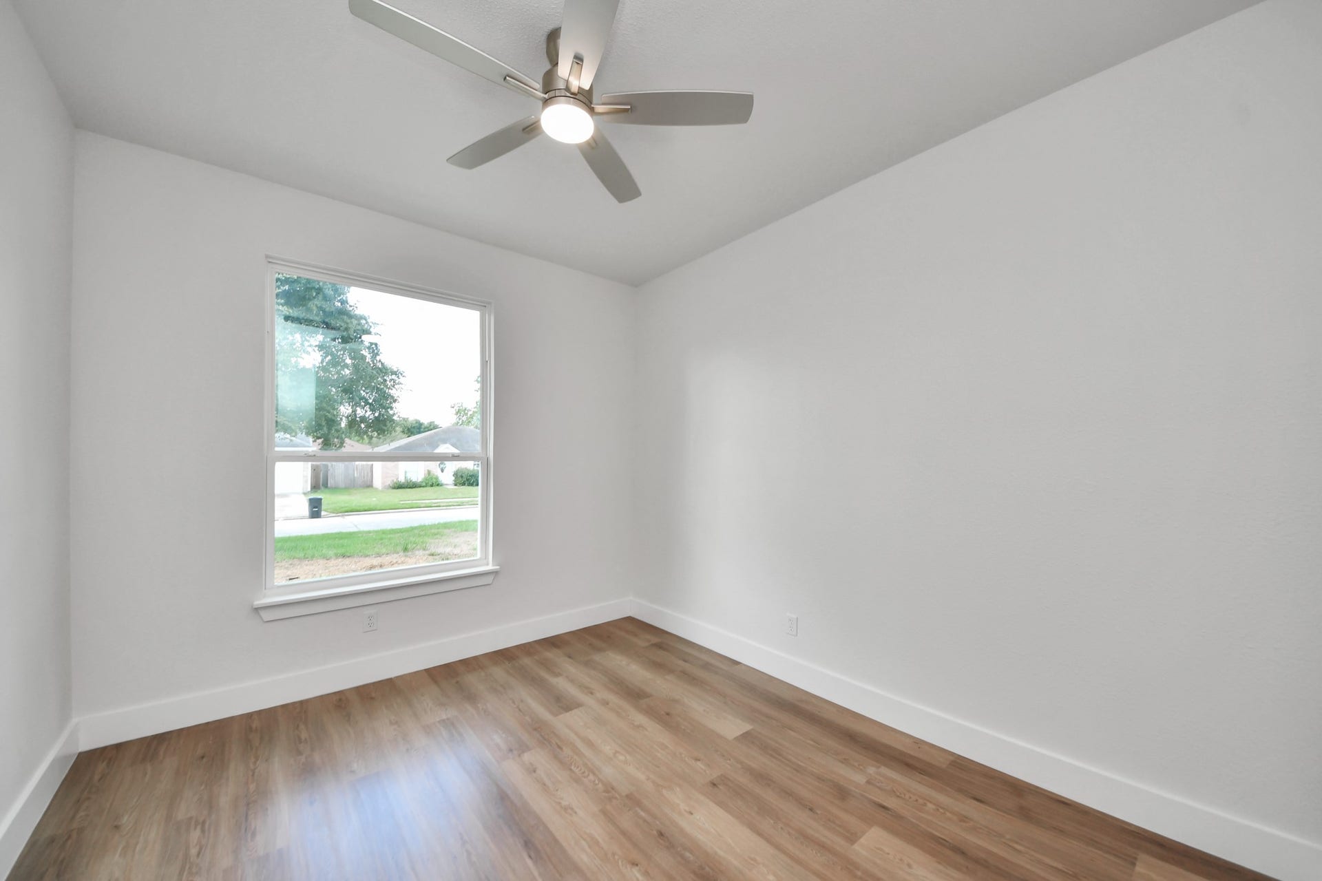 Bright room with sleek hardwood floors, a large window for natural light, and a modern ceiling fan.