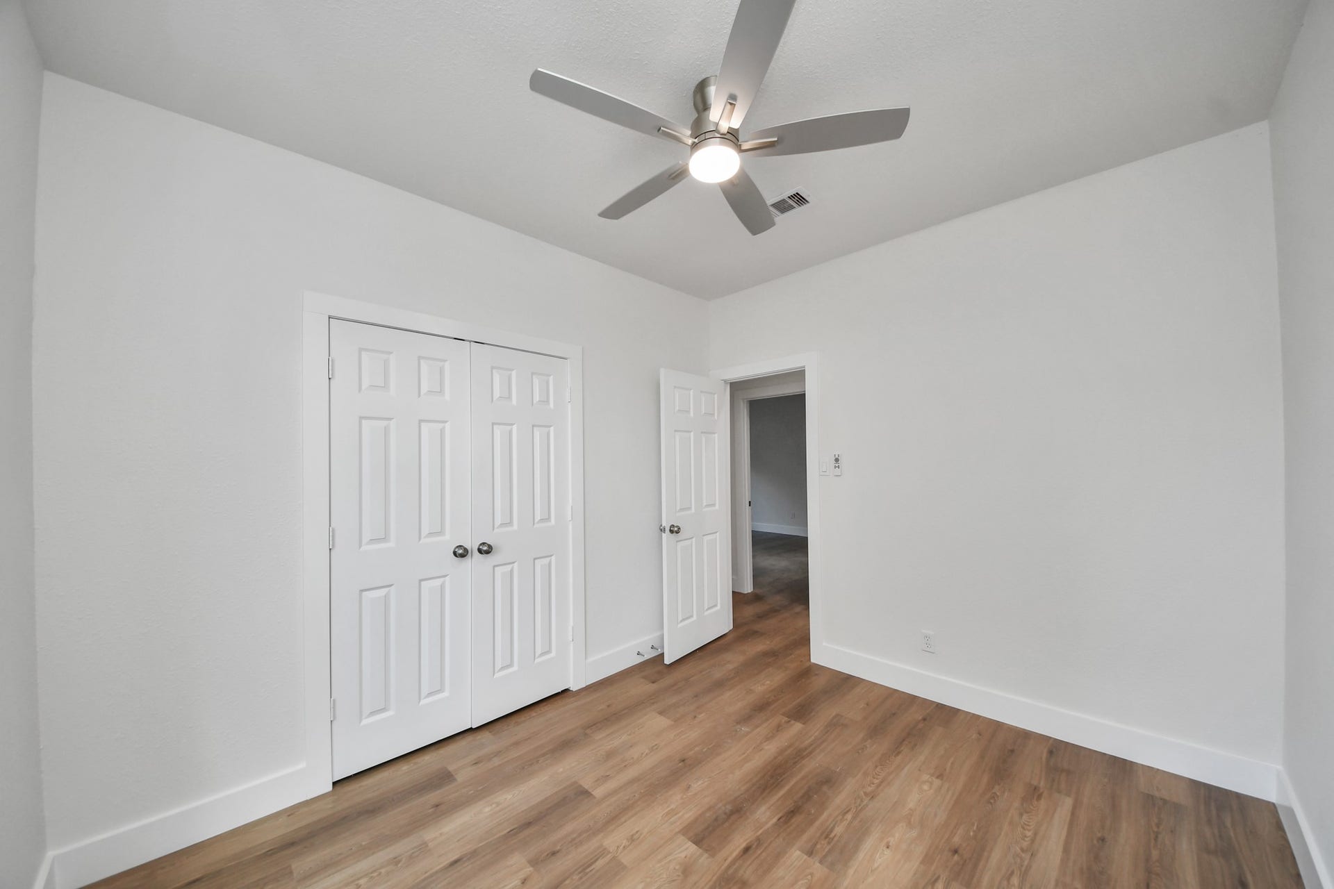 Bright and inviting room featuring fresh white walls, warm wood flooring, and a modern ceiling fan, complemented by convenient double-door closet space.